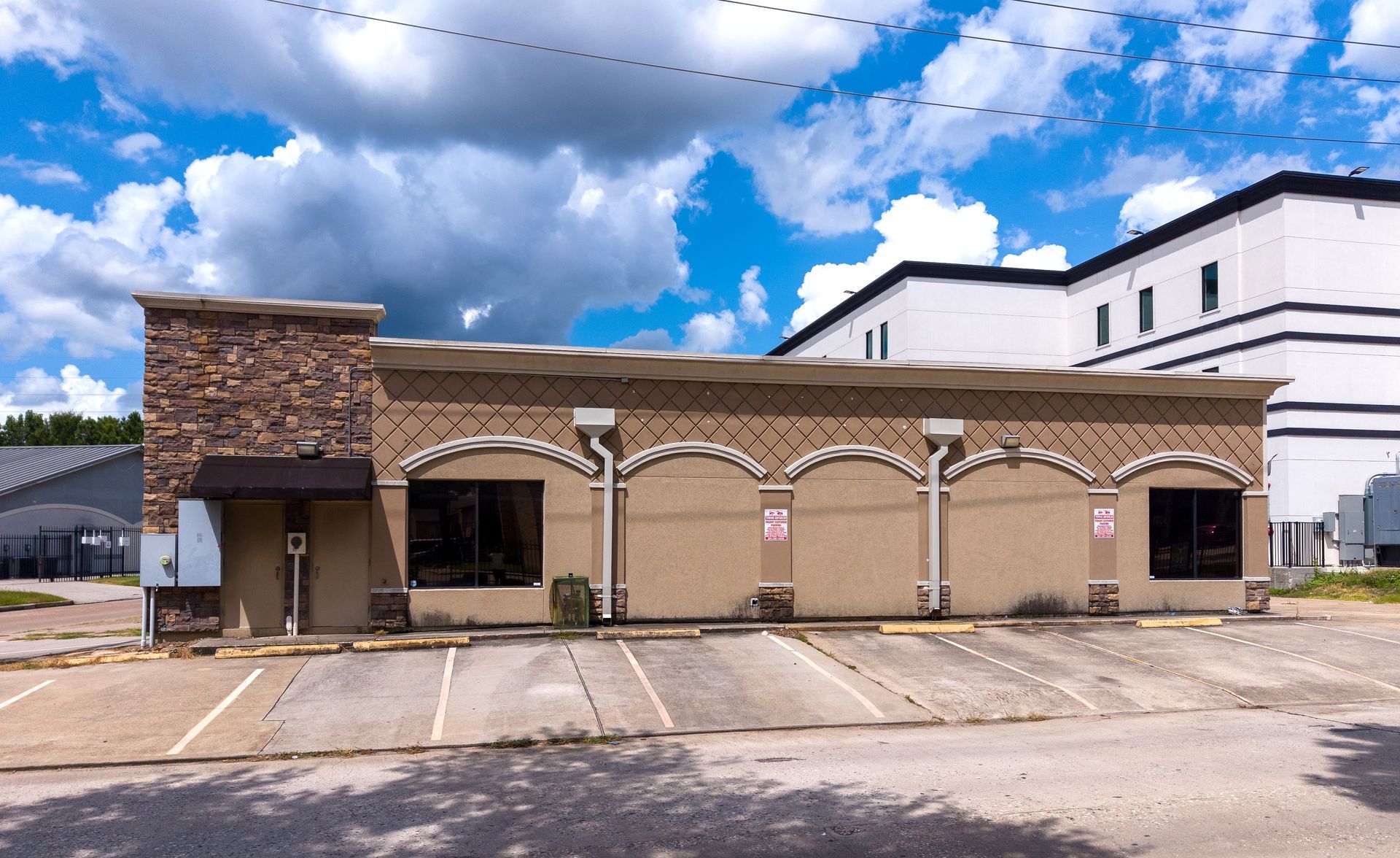 Storefront with stone facade and arched awning under a cloudy blue sky