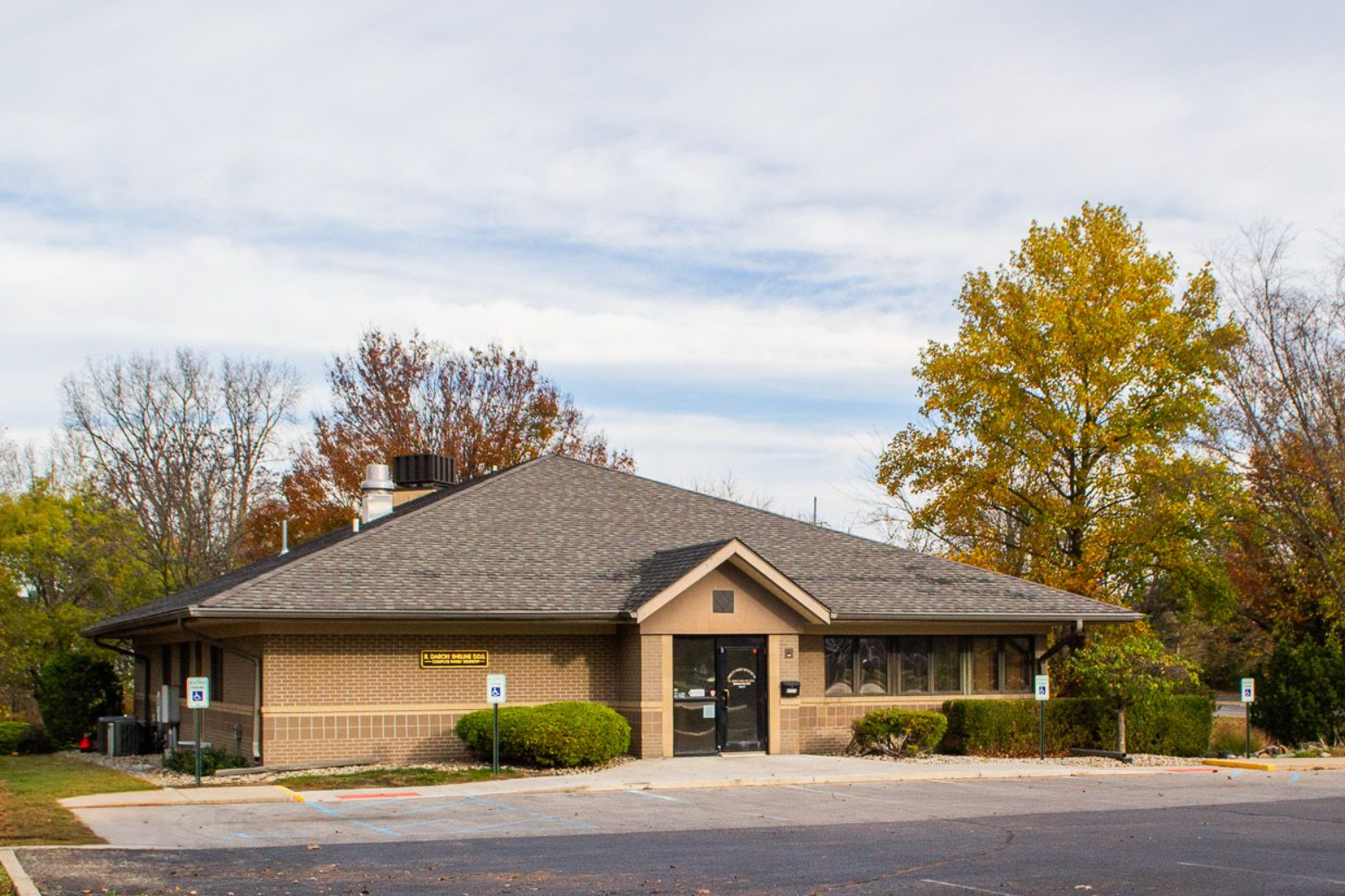 A small building with a gray roof and a parking lot in front of it.