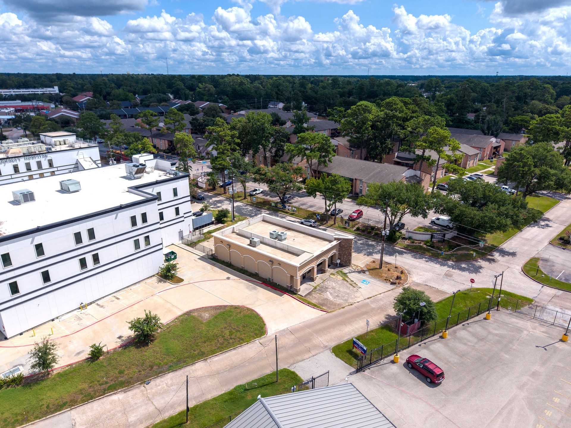Aerial view of a white building, small tan structure, and nearby road with cars under a partly cloudy sky
