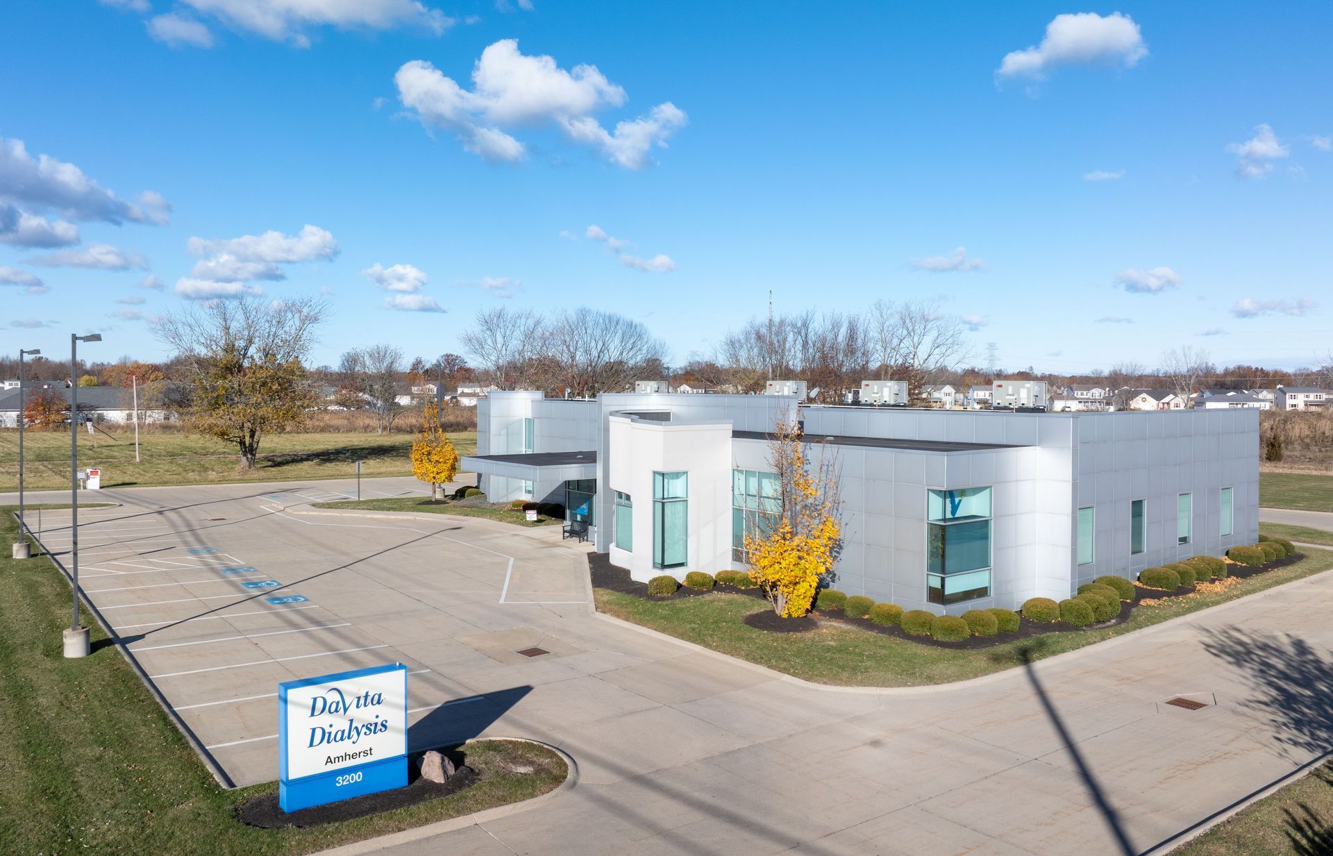 Aerial view of a white DaVita Dialysis building with teal accents and a sign on a sunny suburban street