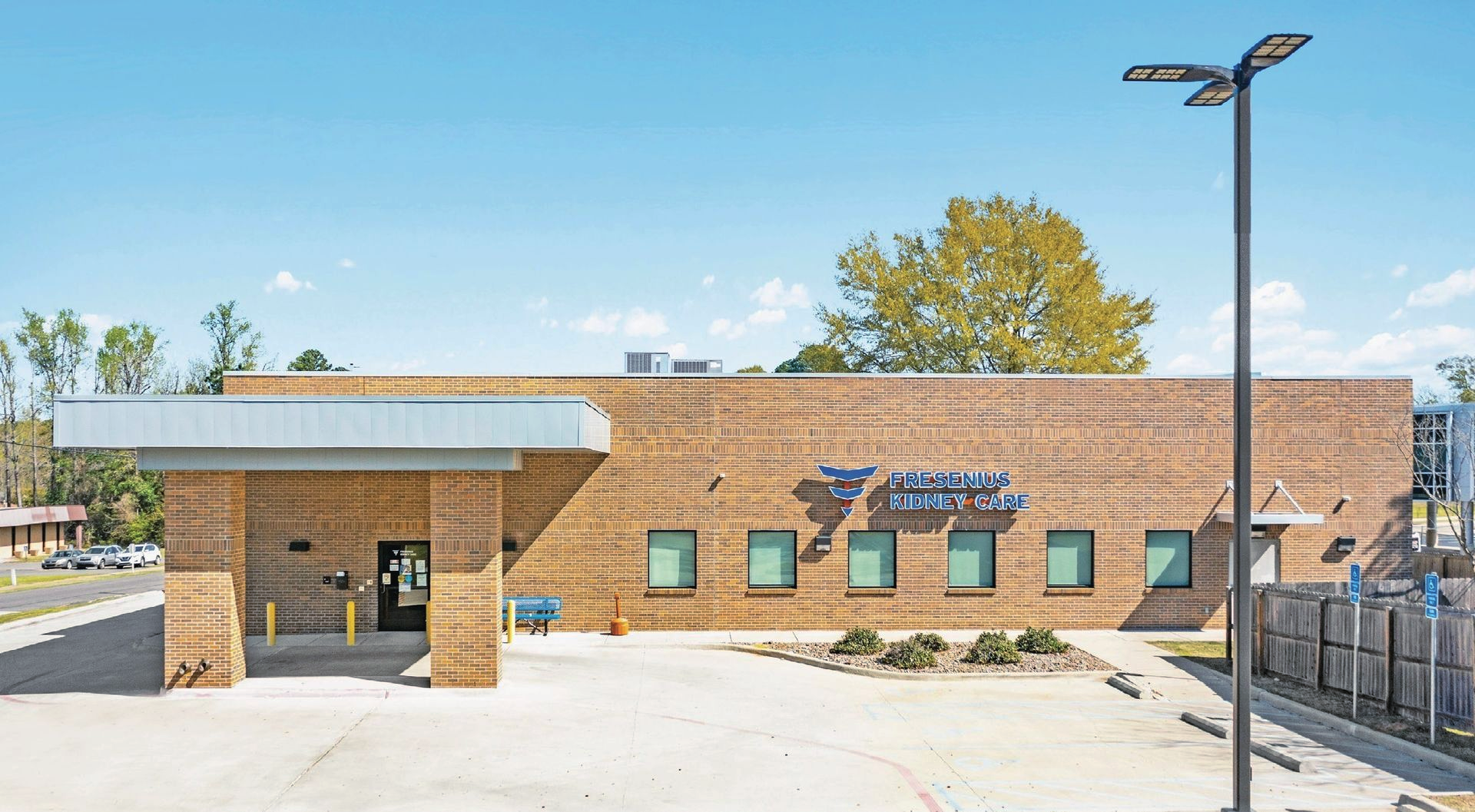 Fresenius Kidney Care dialysis treatment center with blue awning, windows, and parking lot under clear sky