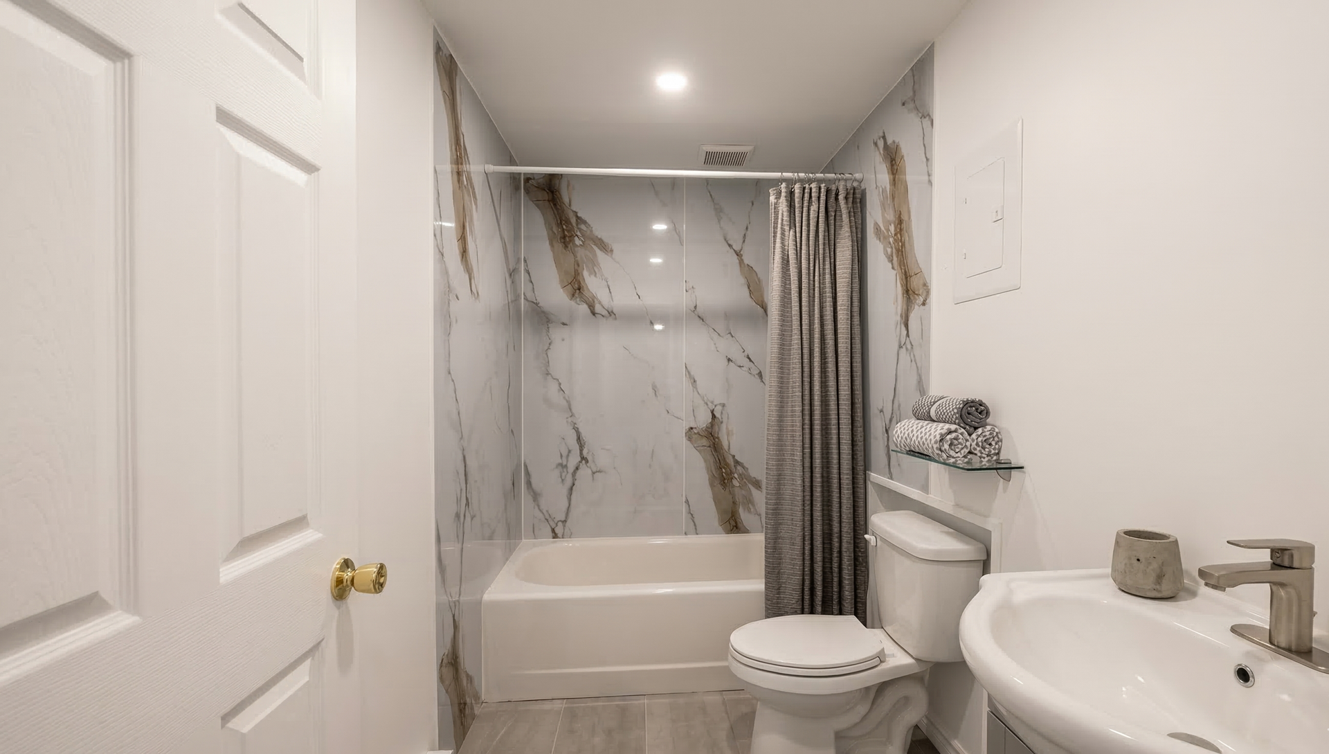 Petite salle de bains avec baignoire, murs à motifs marbrés, toilettes, lavabo sur pied et sol clair.