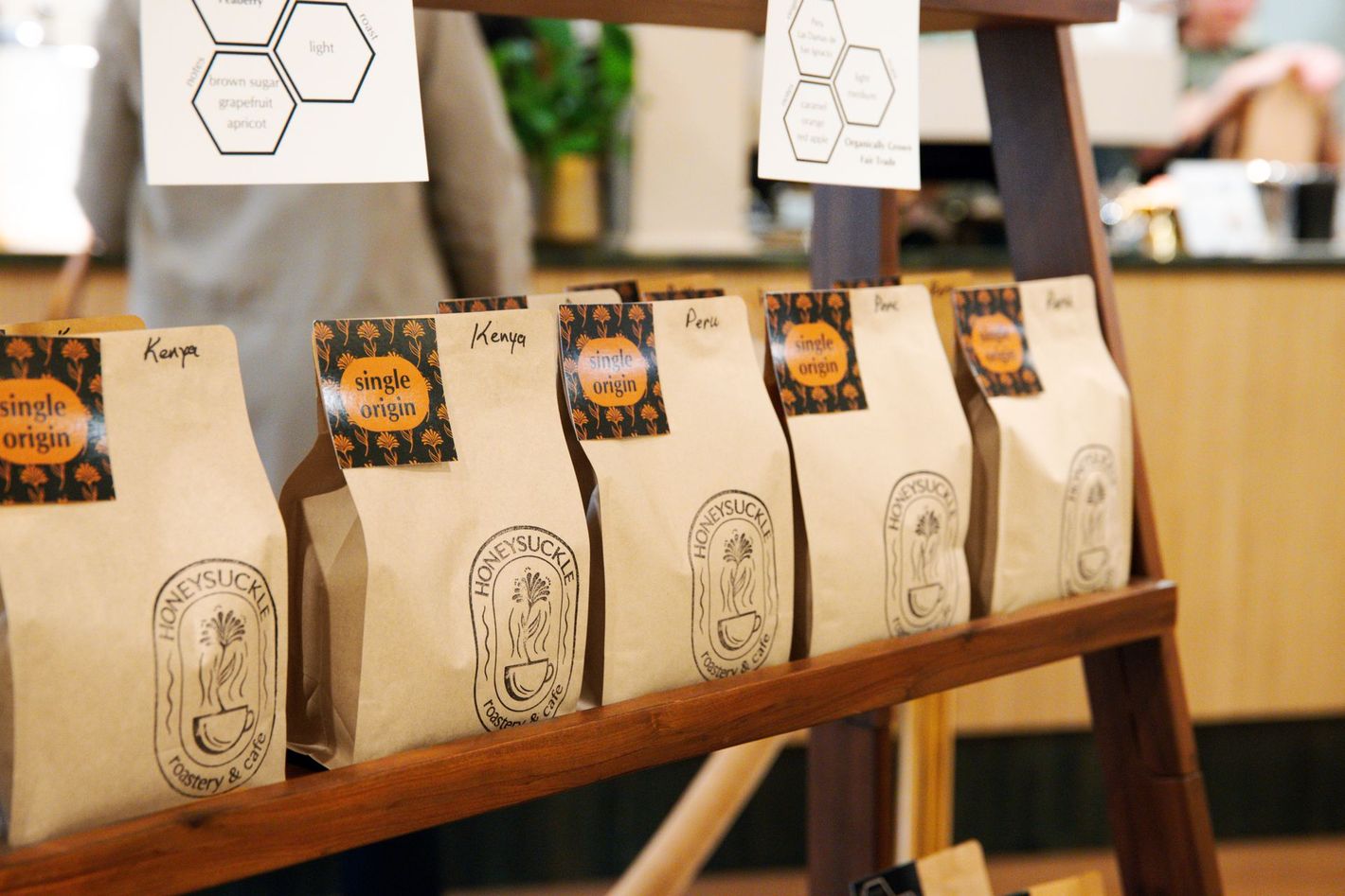 Row of tan coffee bags on a wooden shelf in a cafe display