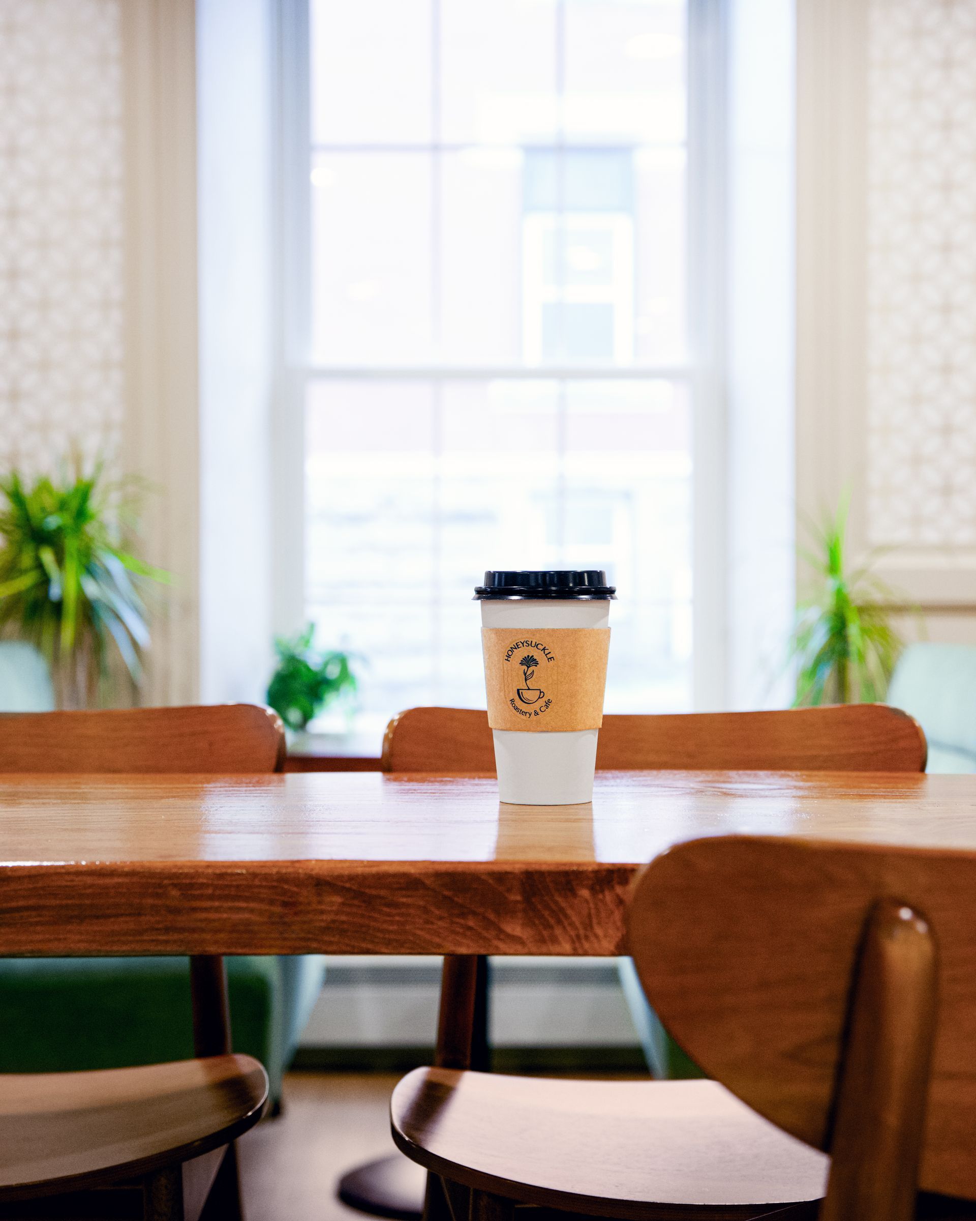 Coffee cup on a wooden table in a bright café with chairs and sunlit windows.
