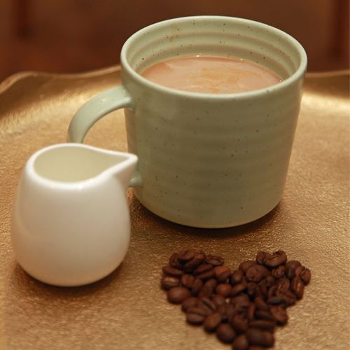 A cup of coffee next to a pitcher of milk and coffee beans in the shape of a heart