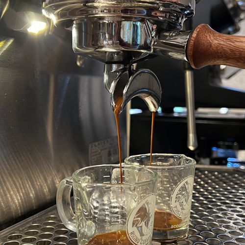 Two cups of coffee are being poured from an espresso machine.