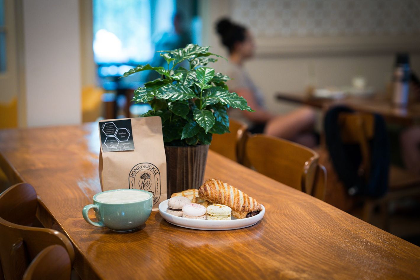 Coffee and pastry on a wooden cafe table with a potted plant and menu card