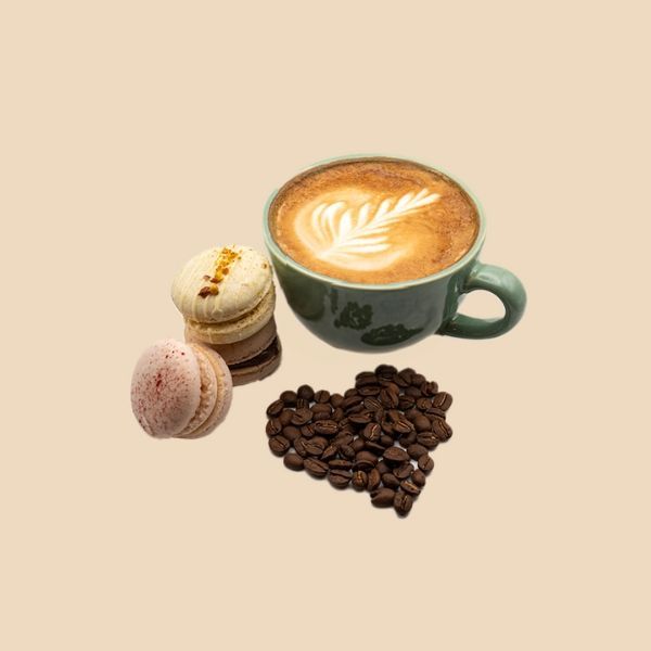 A cup of coffee , macarons , and coffee beans in the shape of a heart.