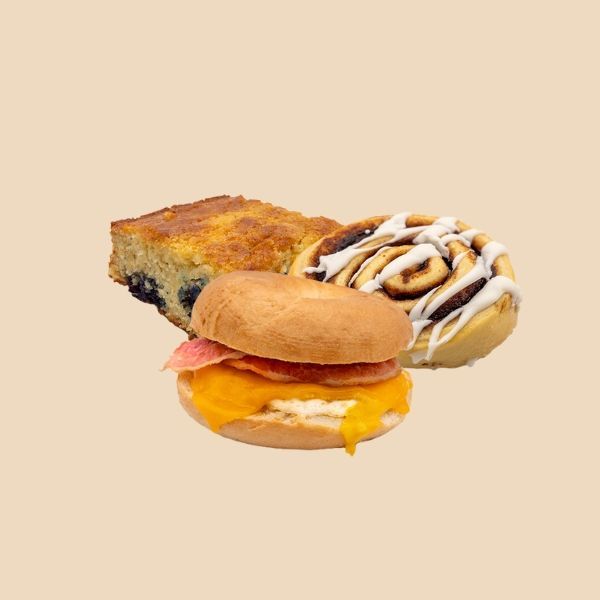 A sandwich , a cinnamon roll , and a blueberry muffin are on a table.