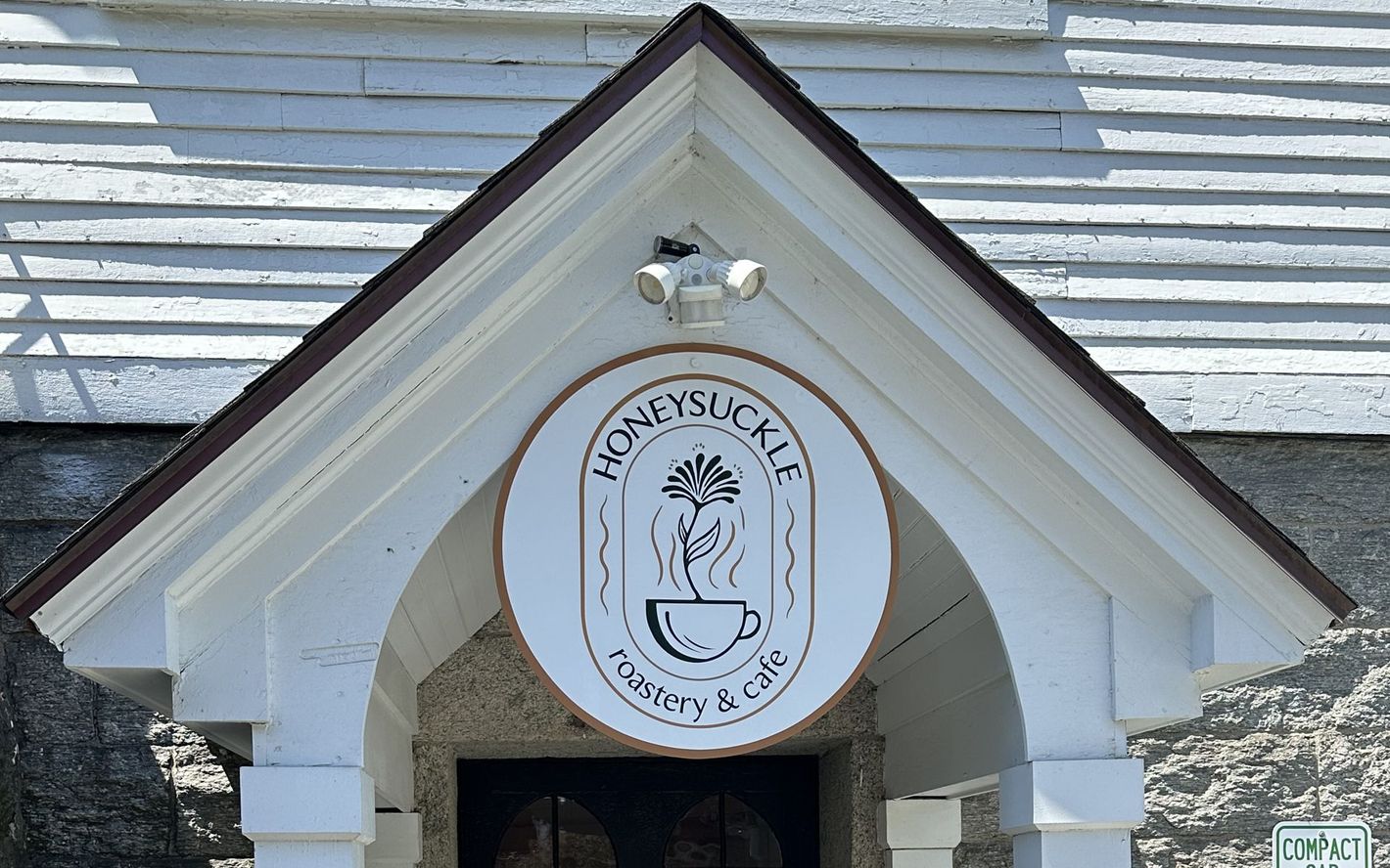 White gabled entrance with a round “Honeysuck...” sign above the doorway and a security light on top
