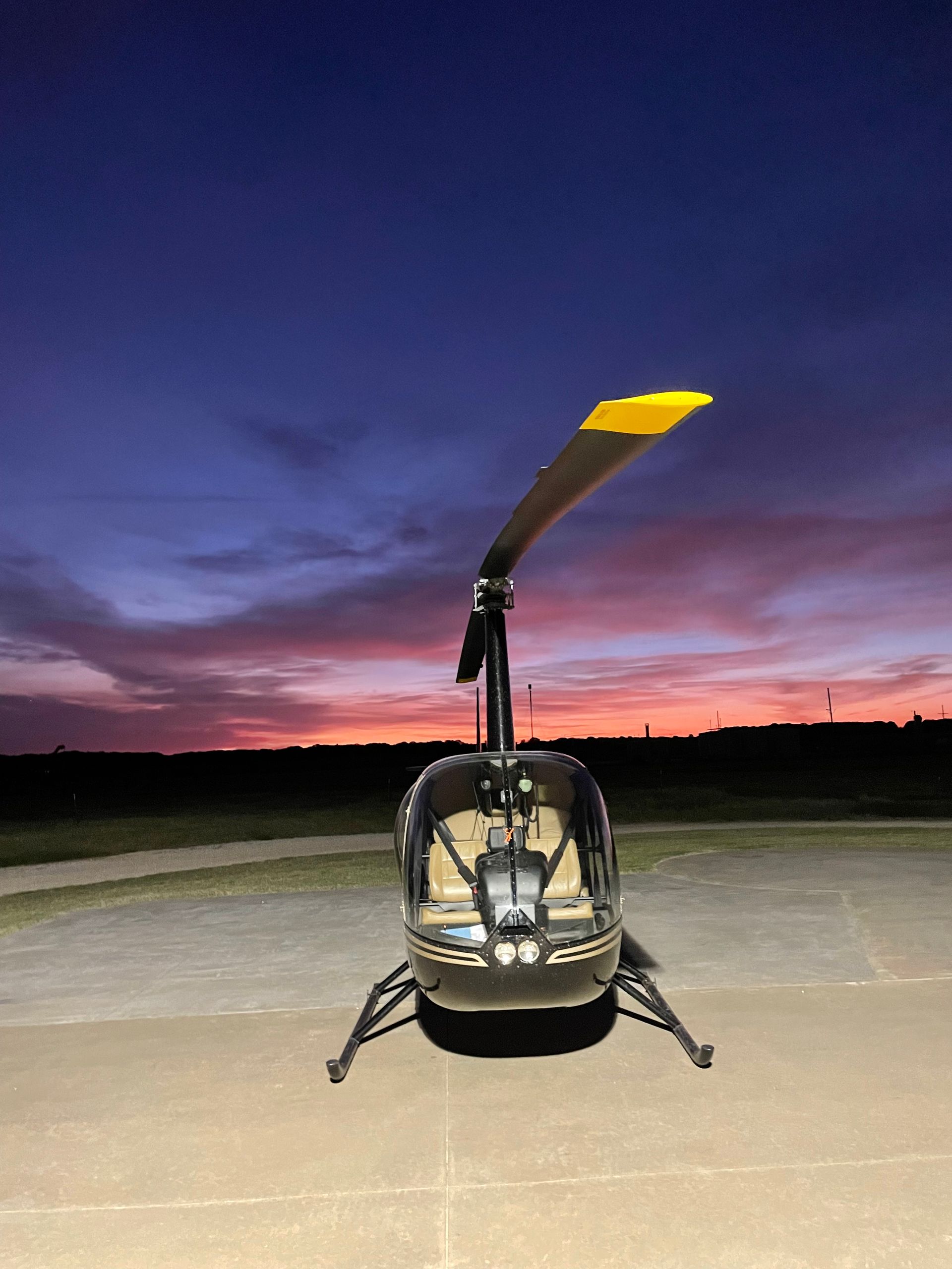 Small helicopter on a runway at dusk, with a purple-orange sunset sky in the background.