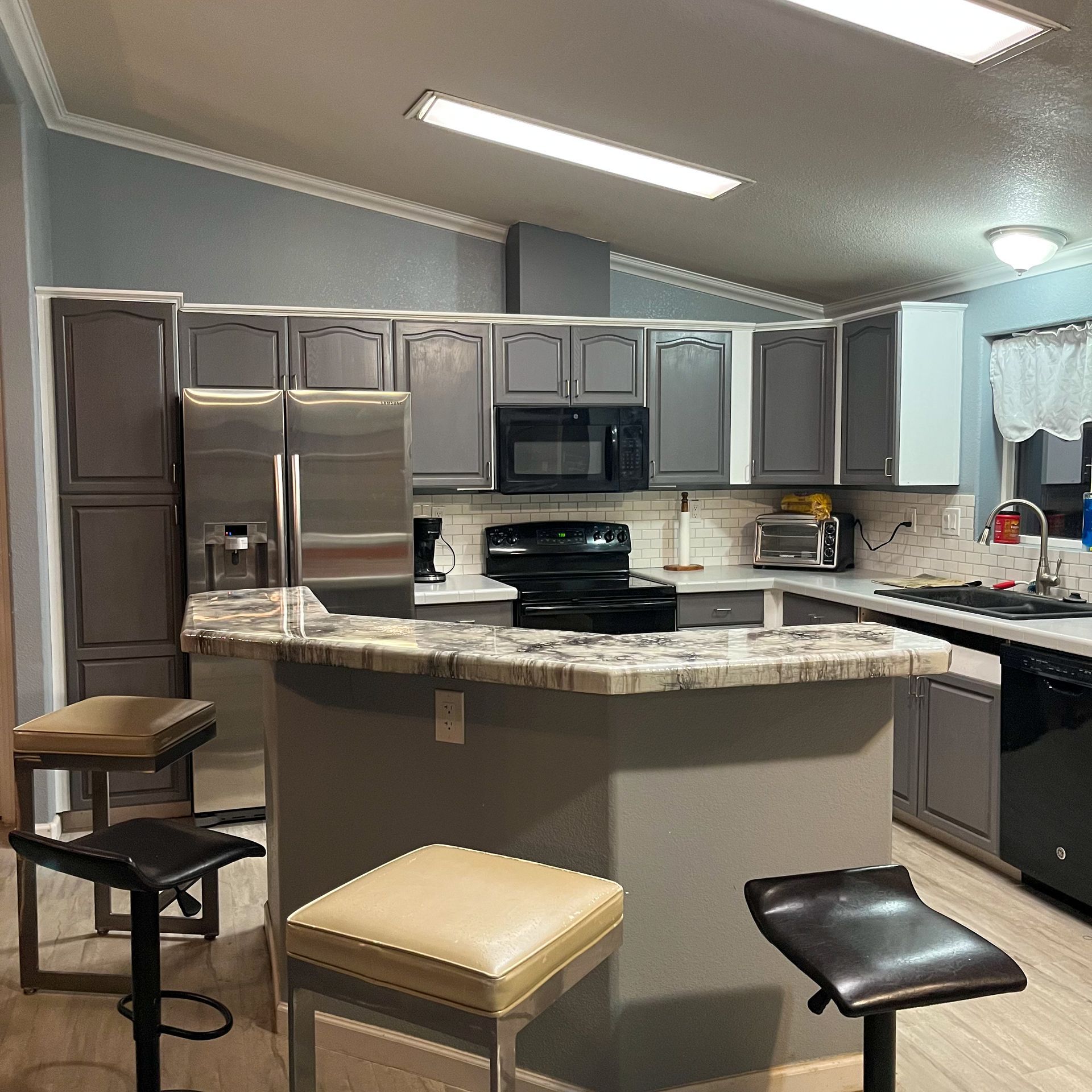 Modern kitchen with gray cabinets, granite island, stainless appliances, and three bar stools