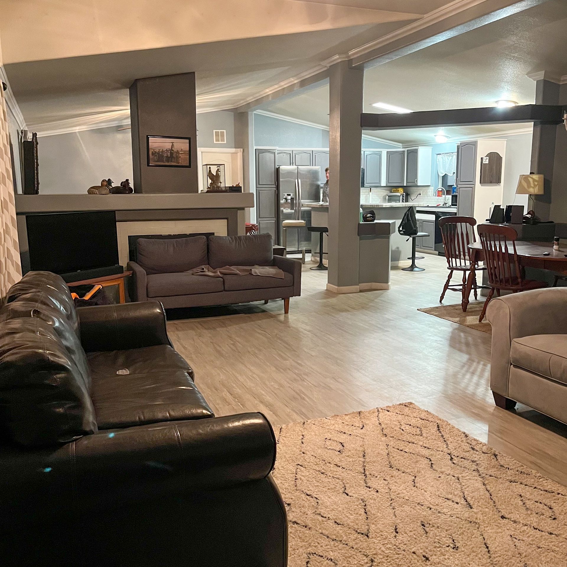 Spacious living room with leather sofas, fireplace, and open kitchen in the background.