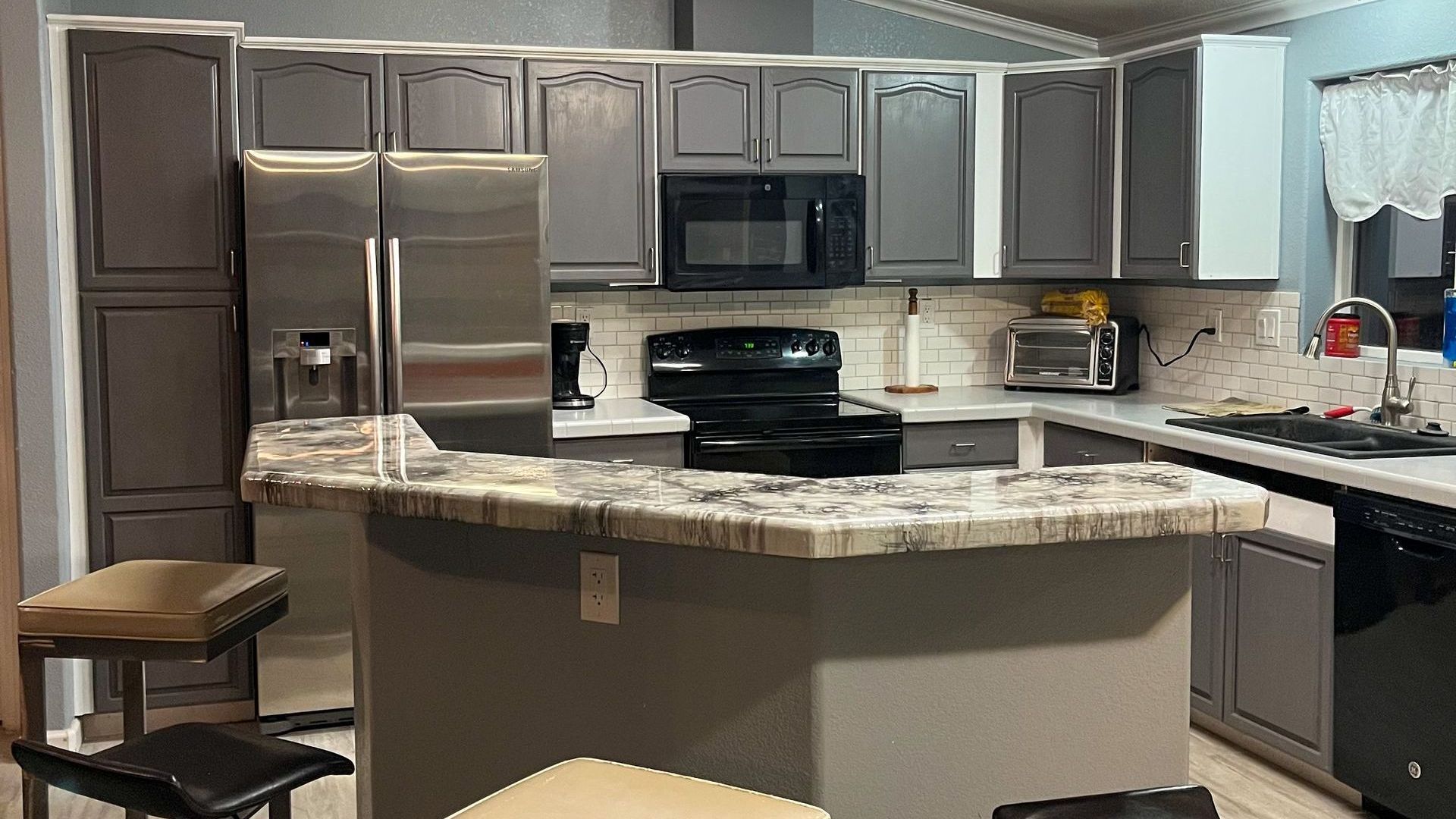 Modern kitchen with gray cabinets, stainless appliances, and a granite island counter