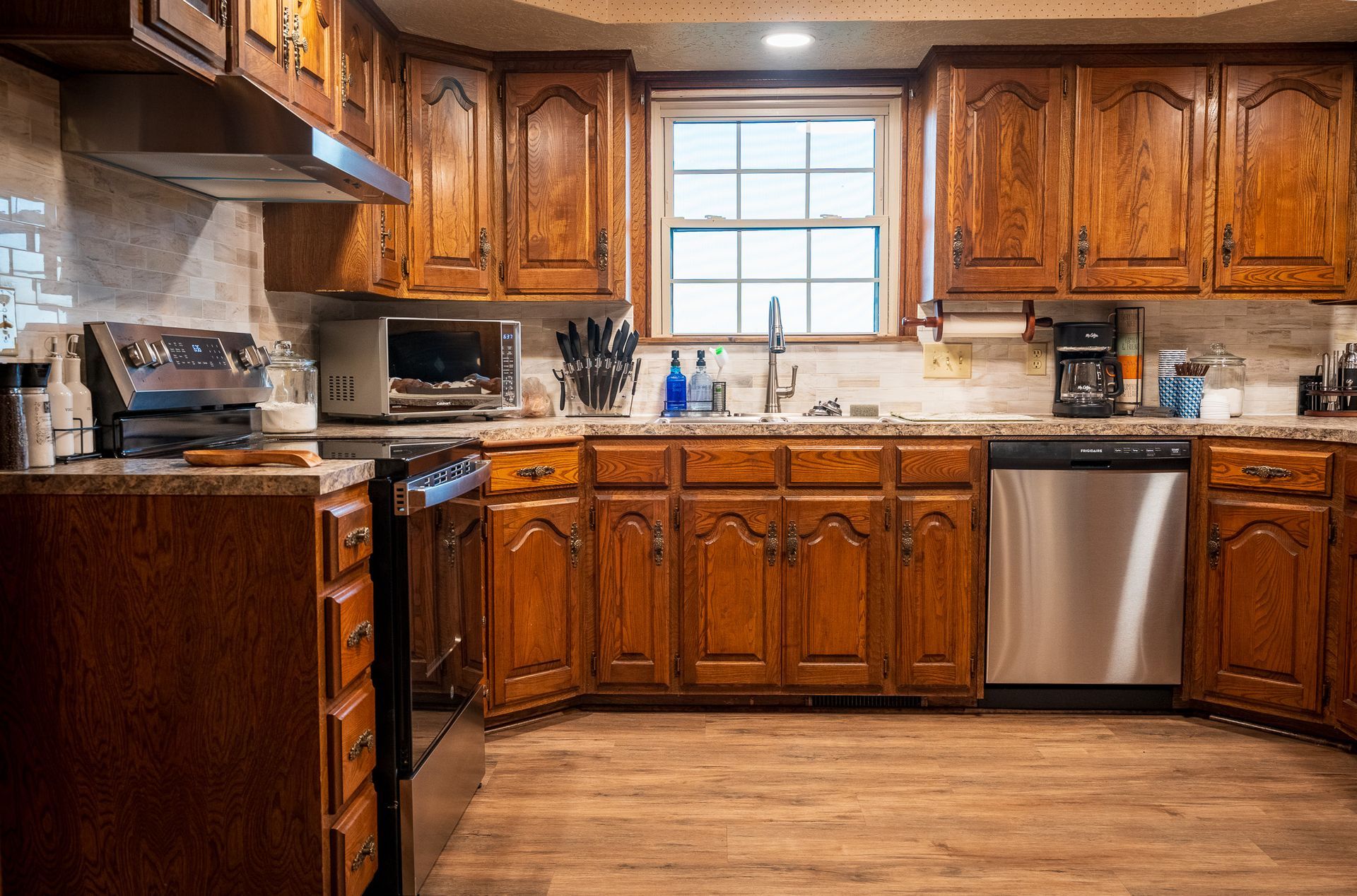 Wooden kitchen with cabinets, granite counters, stainless dishwasher, and a window above the sink.