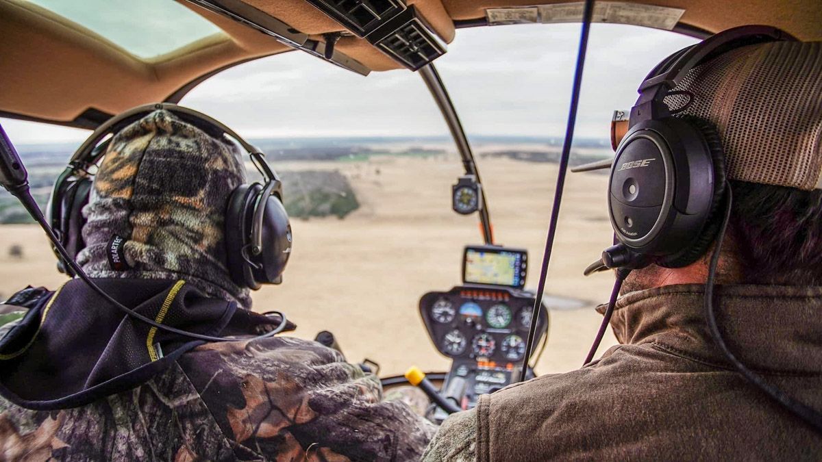 Two headset-wearing pilots in a helicopter cockpit, flying over a desert landscape.