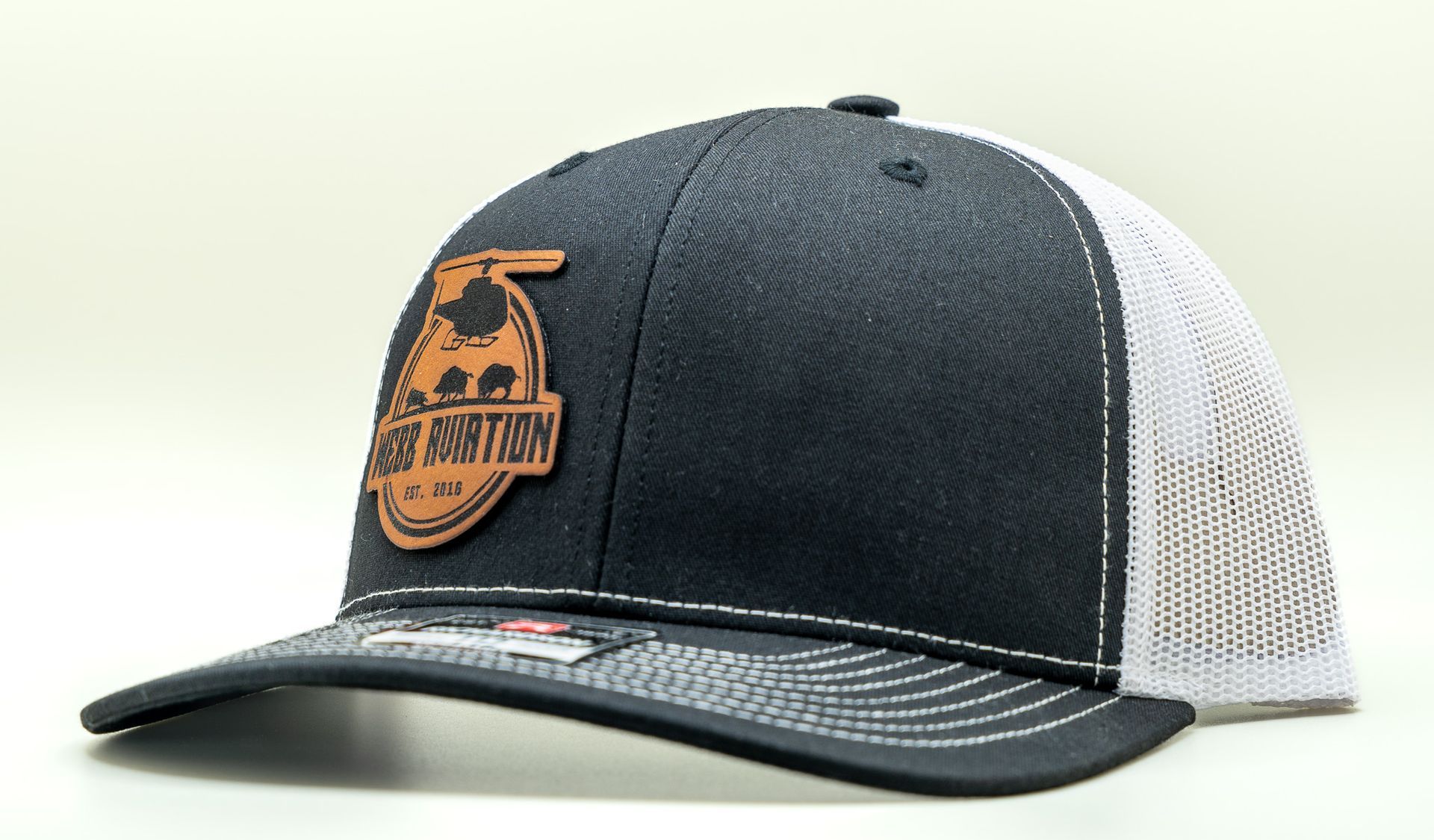Black and white mesh trucker cap with a tan logo patch on the front, shown on a white background