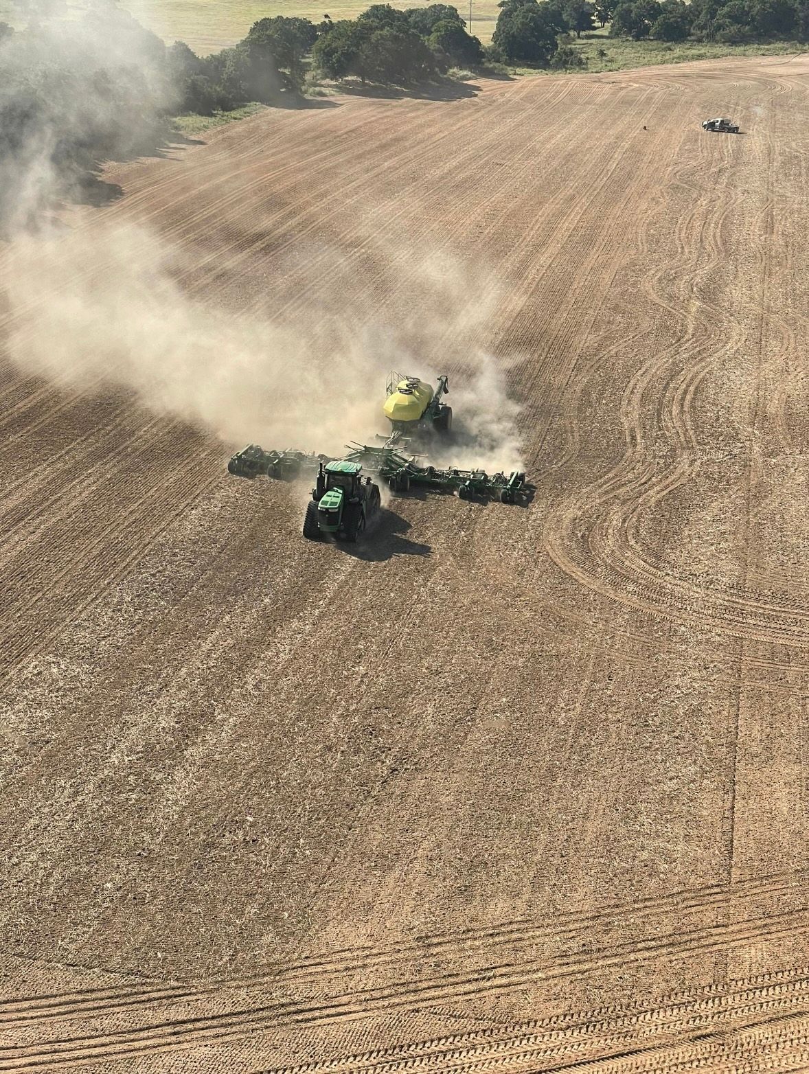 Two green combines harvesting a dry field, kicking up dust from the crop.