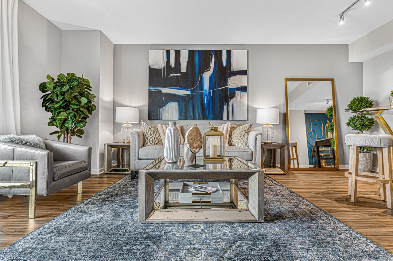 Bright, modern living room featuring a sleek gray sofa, glass coffee table, abstract art, and lush greenery at Olympus Harbour Island, offering apartments in Tampa, FL.