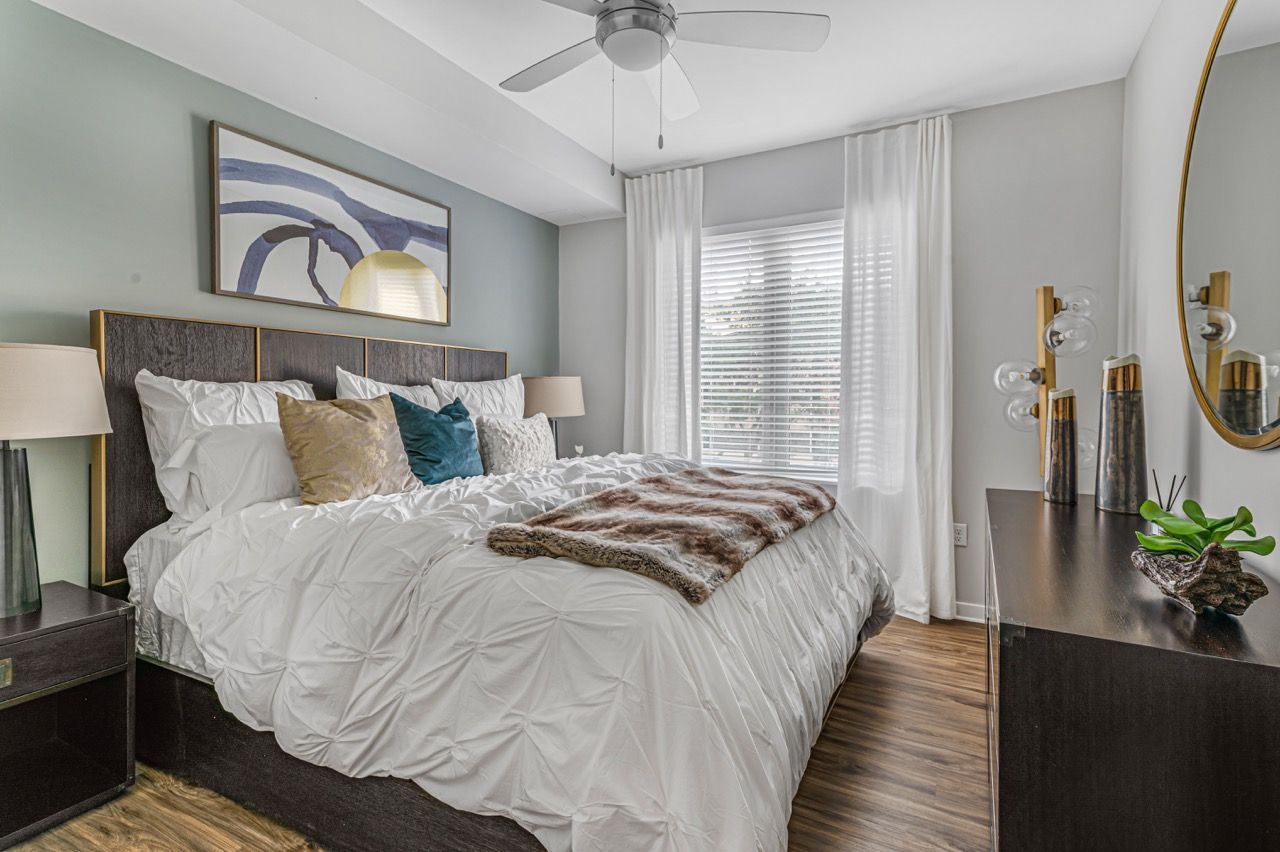 Bedroom in an apartment Olympus Harbour Island, offering apartments in downtown Tampa, FL, featuring a white tufted comforter, decorative pillows, and a dresser beside a window.