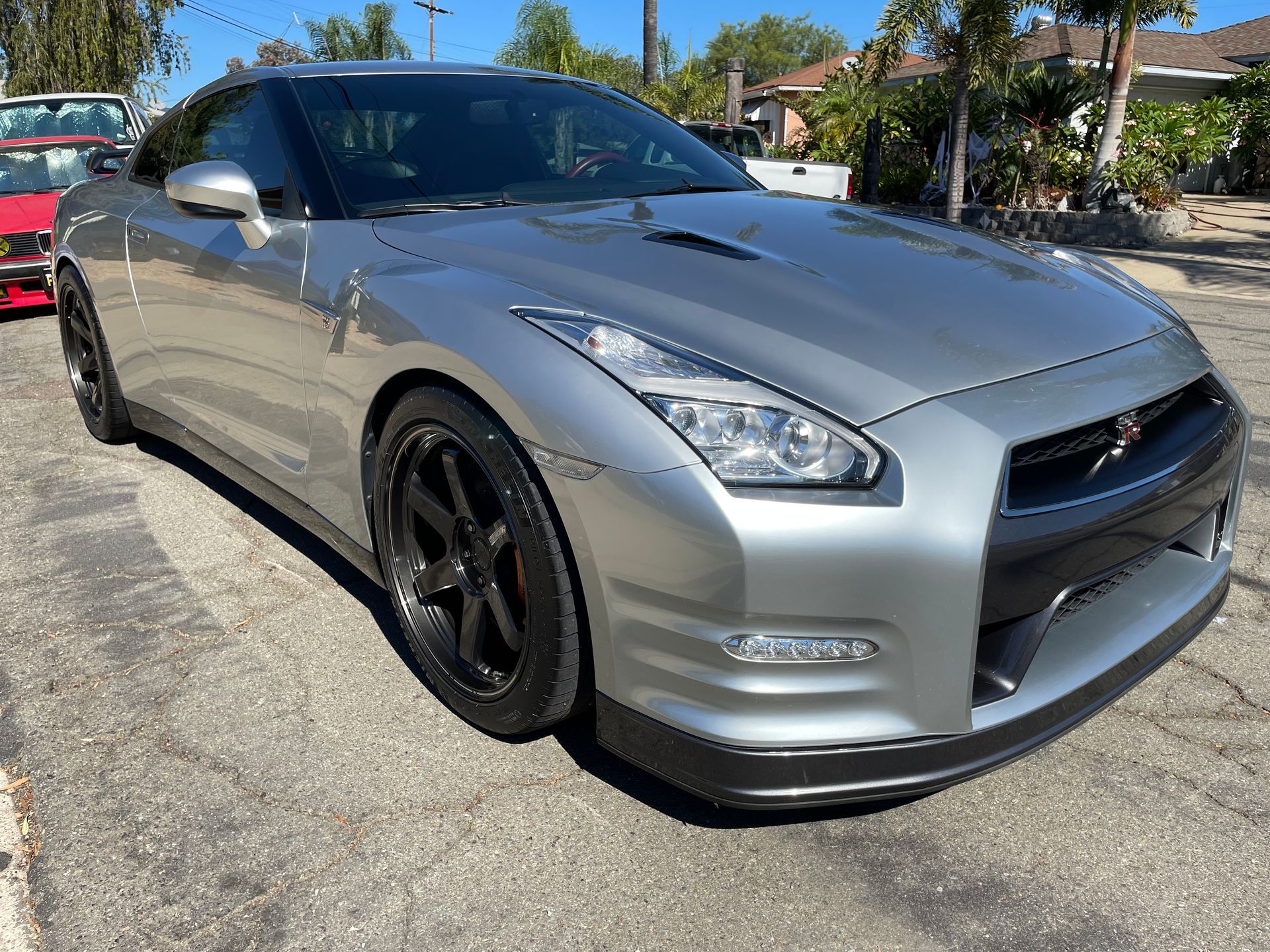 Silver Nissan GT-R sports car parked on asphalt, sunny day. Black wheels, sleek design.