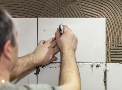 A man is laying tiles on a wall with a hammer.