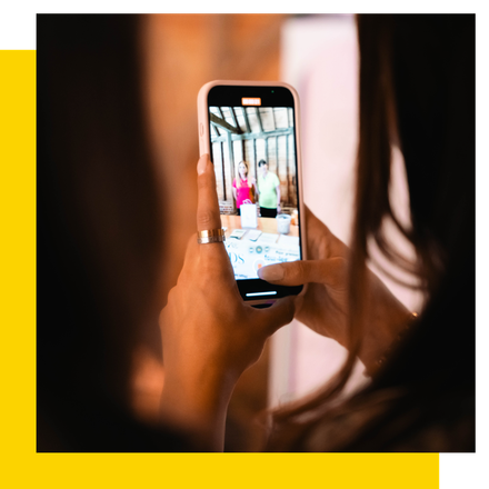 Person holding a phone, taking a photo of two people behind a table.