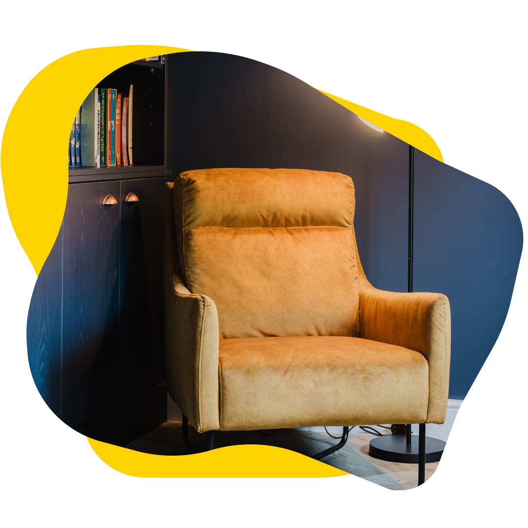 Yellow armchair in a room with dark blue walls, next to a black cabinet with books.