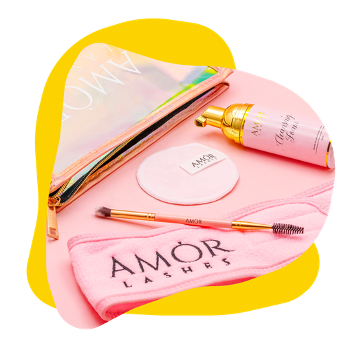 Pink Amor Lashes beauty set with a clear cosmetic bag, cleanser, pads, brush, and headband on a pink backdrop.