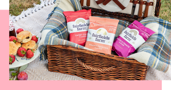 Picnic basket with snacks: muffins, three colorful nut packs, and a blanket.