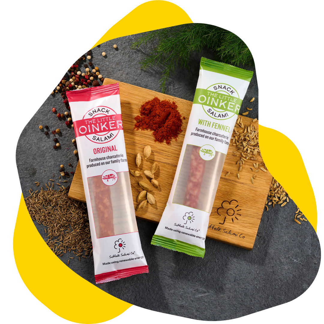 Two sausage sticks in colorful packaging on a wooden board with spices, herbs, and yellow graphic.