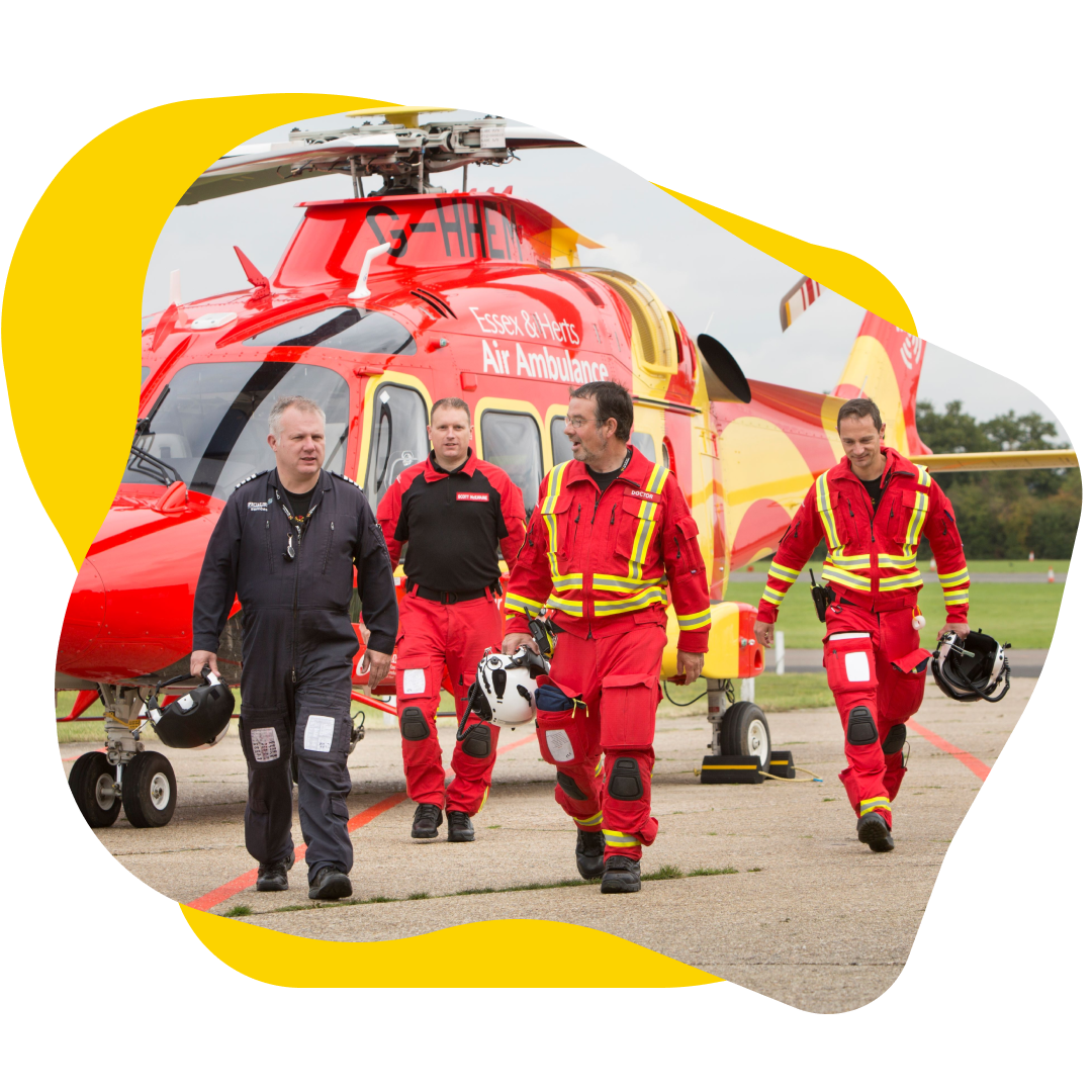 Four people in red uniforms walking in front of a red and yellow helicopter.
