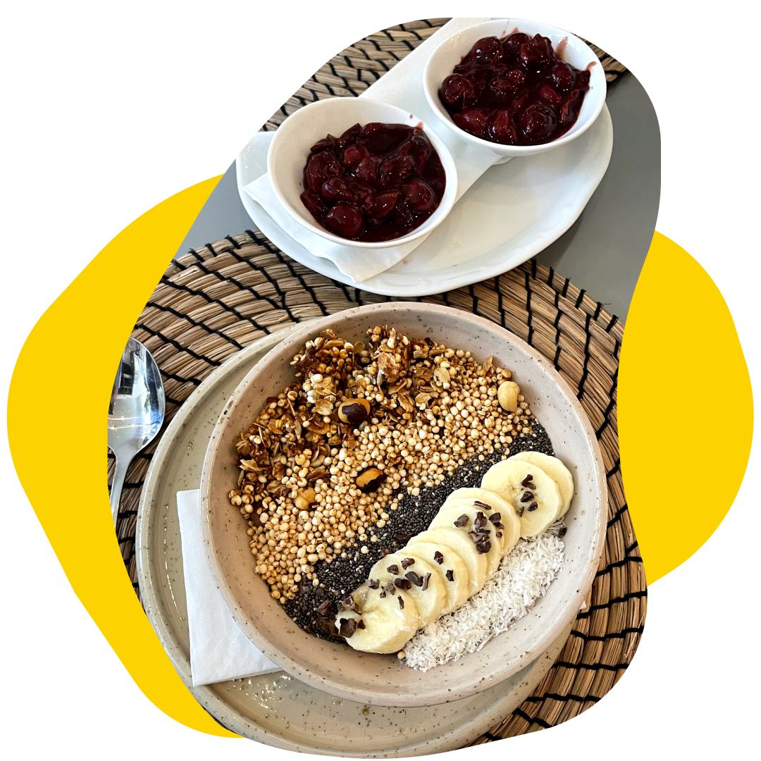 Granola bowl with banana slices, berries, and a side of cherries.