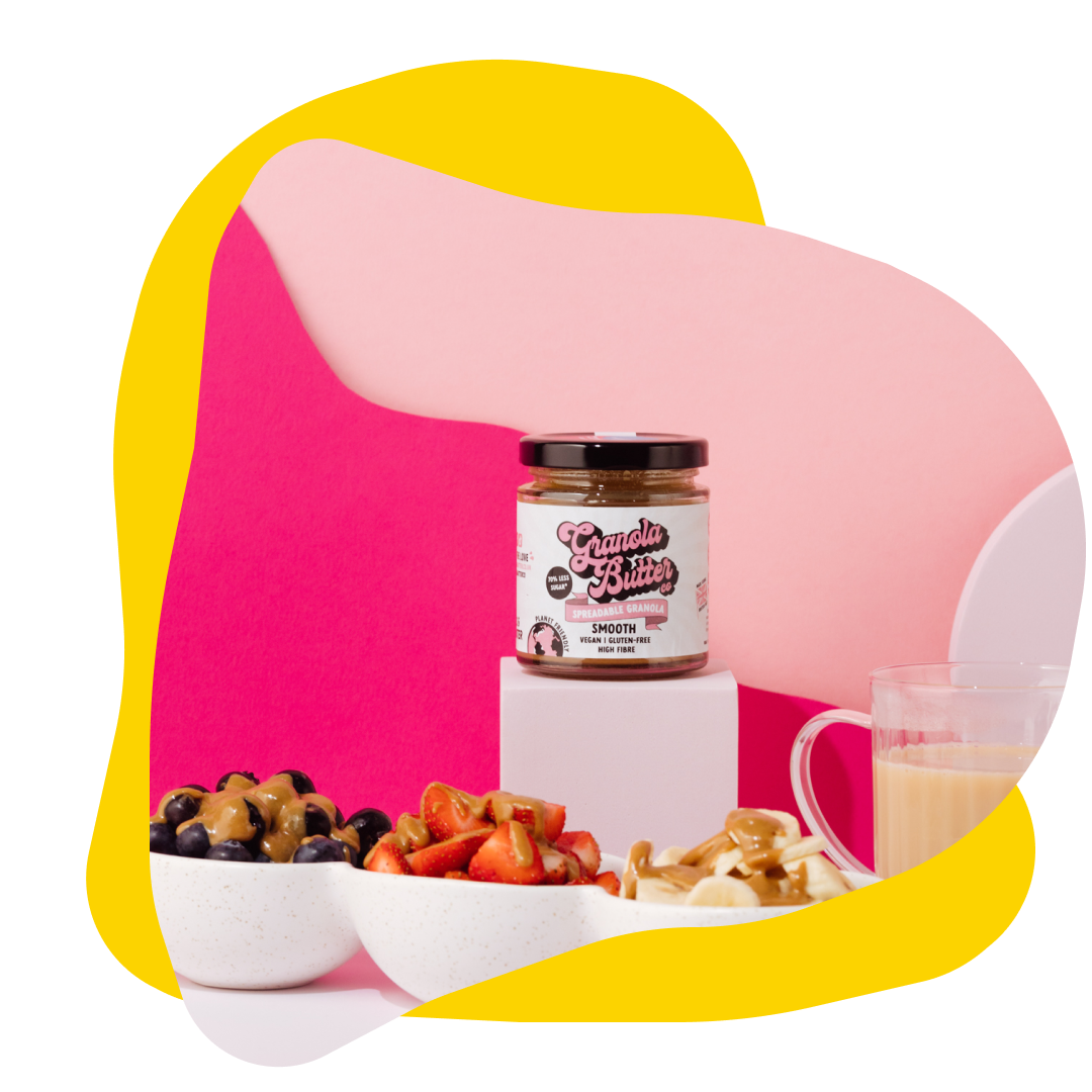 A jar of nut butter and bowls of fruit with toppings on a pink and yellow background.