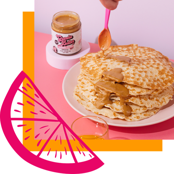 Stack of pancakes with nut butter being drizzled from a pink spoon, jar of nut butter, and a pink citrus graphic.