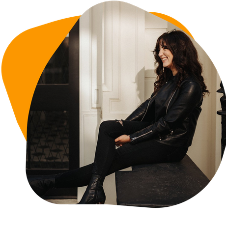 Woman in black jacket and jeans, sitting and smiling.
