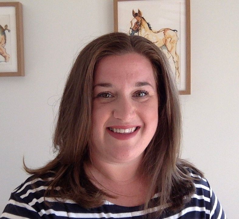 Woman with brown hair smiles, wearing a striped shirt. Paintings of horses in the background.