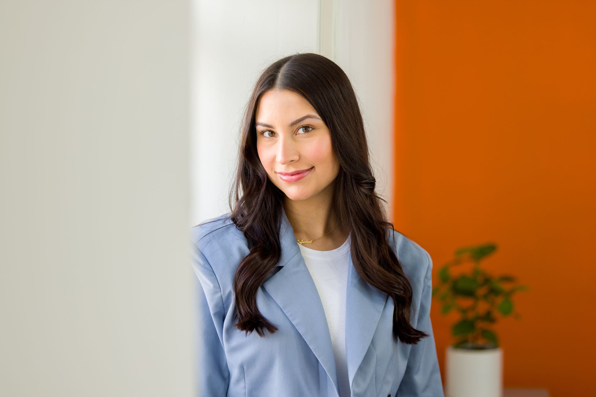 Woman in blue blazer smiles, leans against white and orange wall.