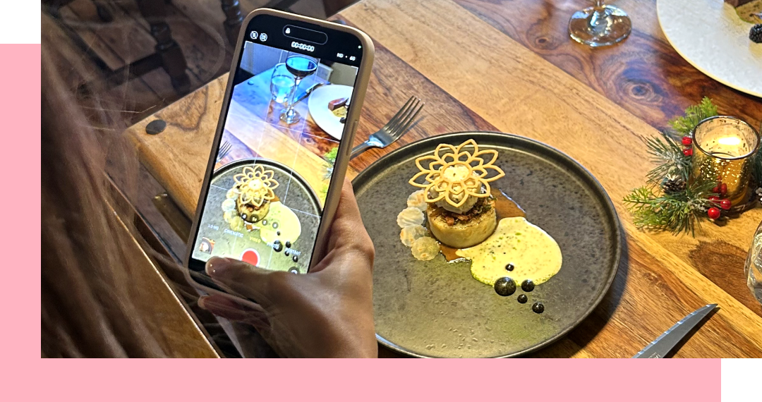 A hand holding a phone taking a photo of plated dessert on a wooden table.