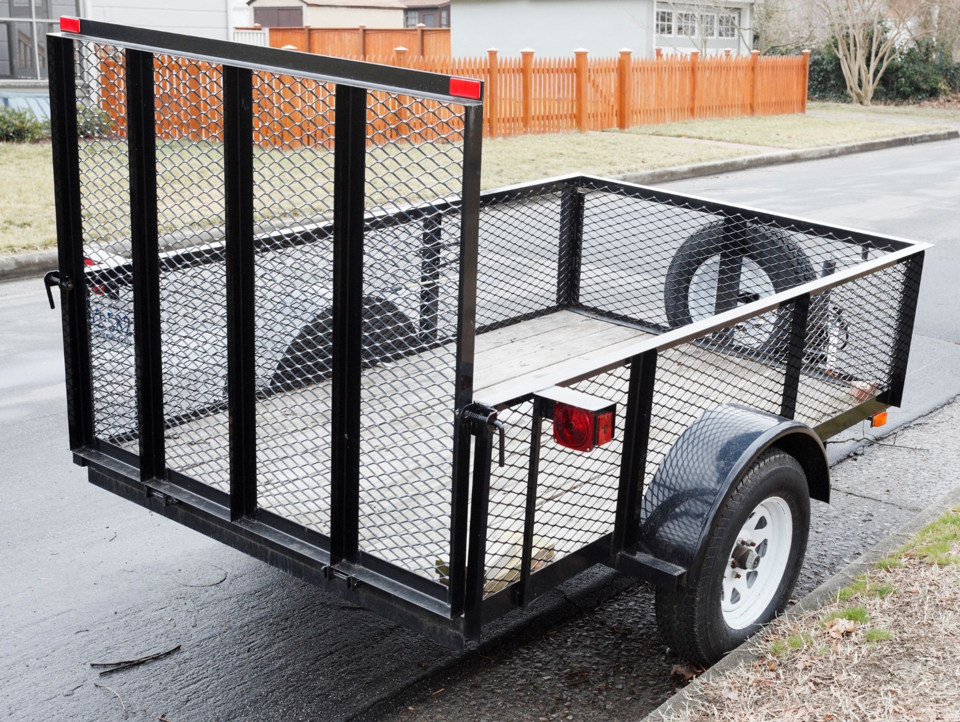 Black utility trailer with mesh sides and a ramp gate parked on a street