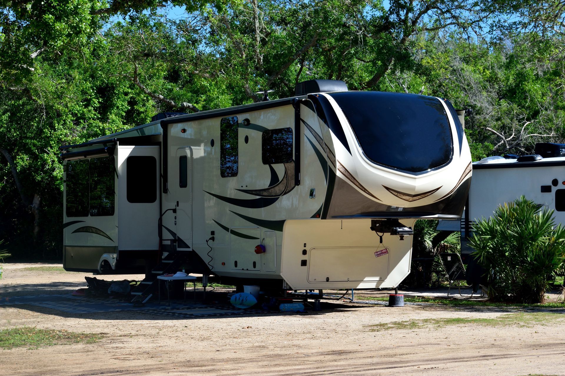 White and tan RV parked on a dirt lot with trees in the background