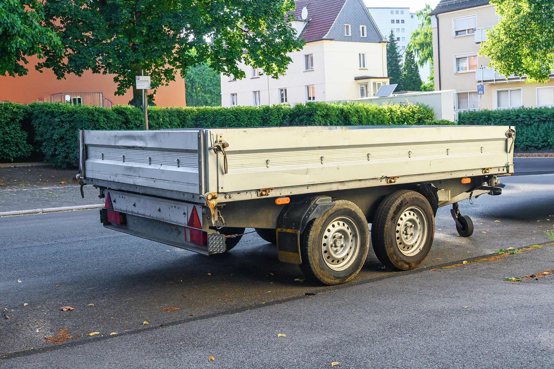Two-axle gray utility trailer parked on a street in a residential area