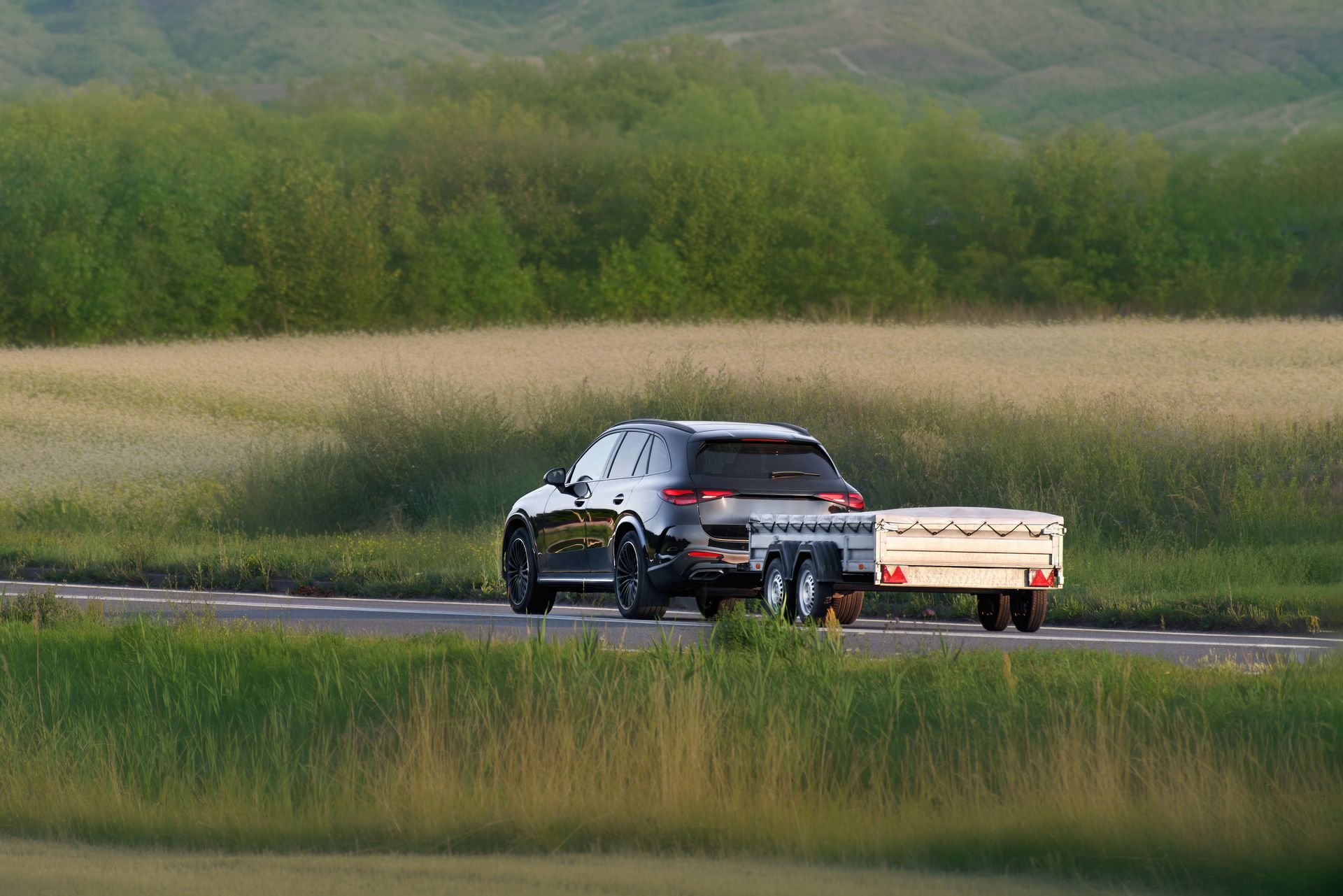 Silver SUV towing a small trailer on a rural road beside grassy fields