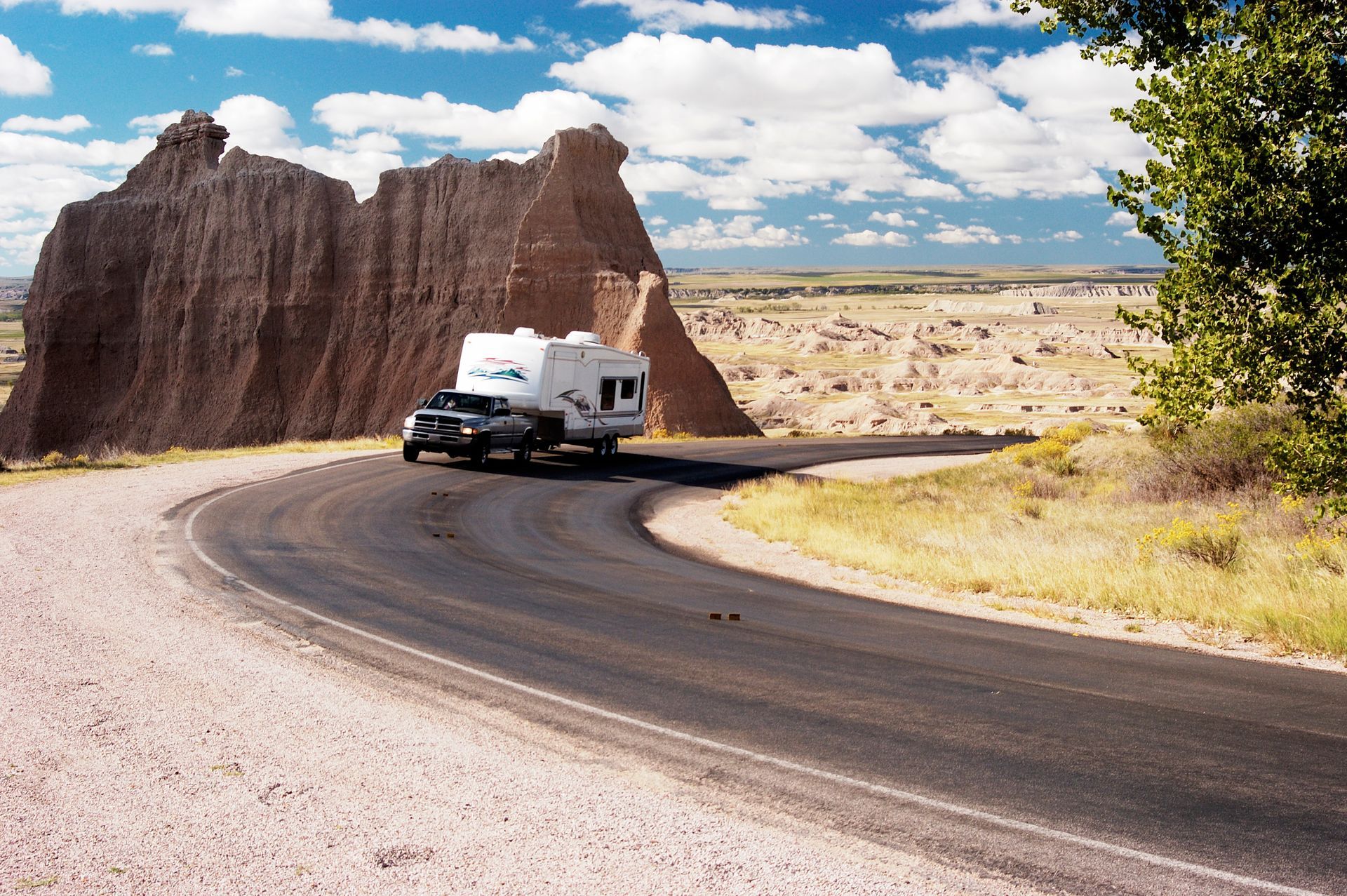 White RV on a winding desert road beside red cliffs under a blue sky