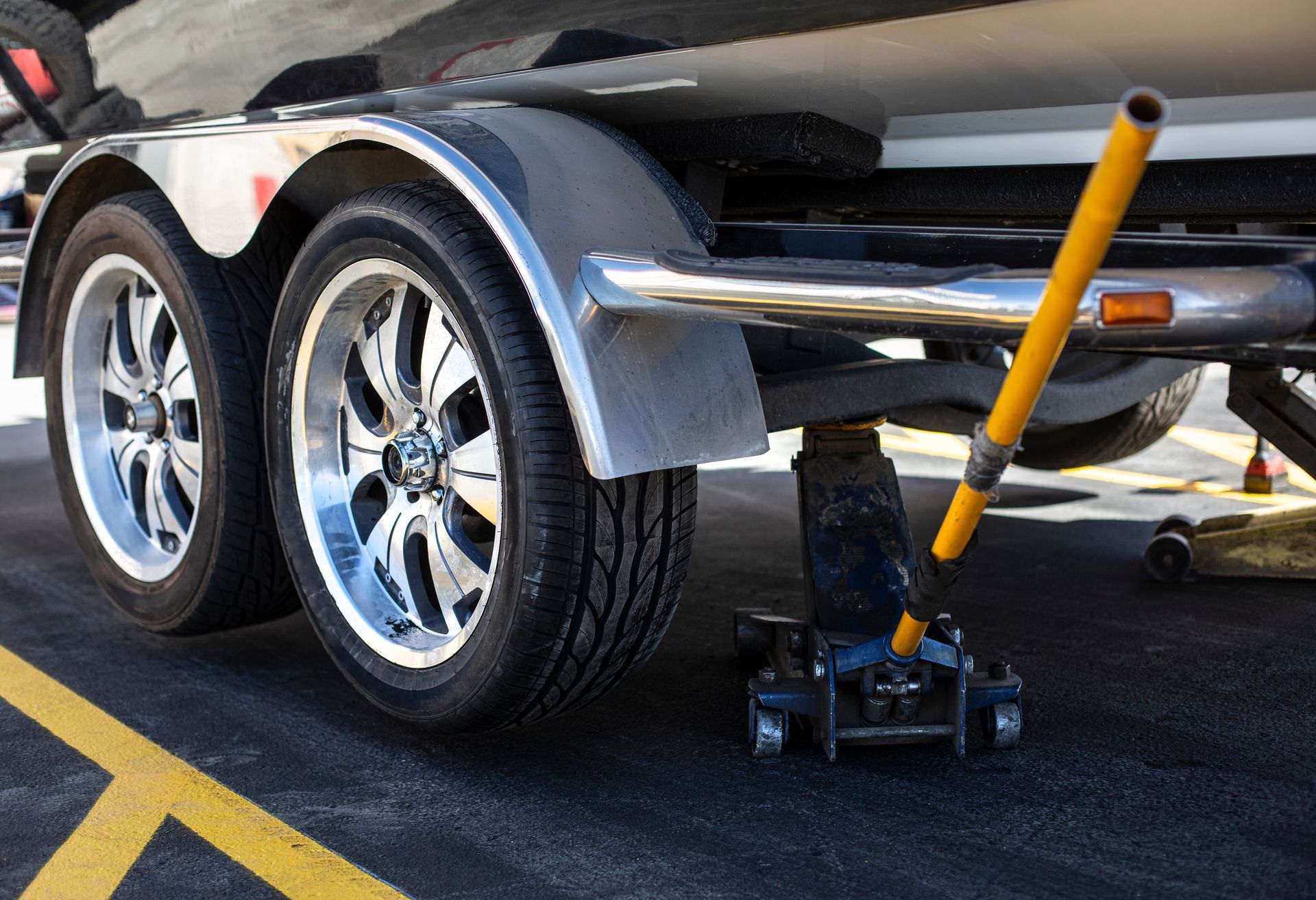 Car on a small floor jack with a yellow handle, parked on asphalt near yellow lane lines