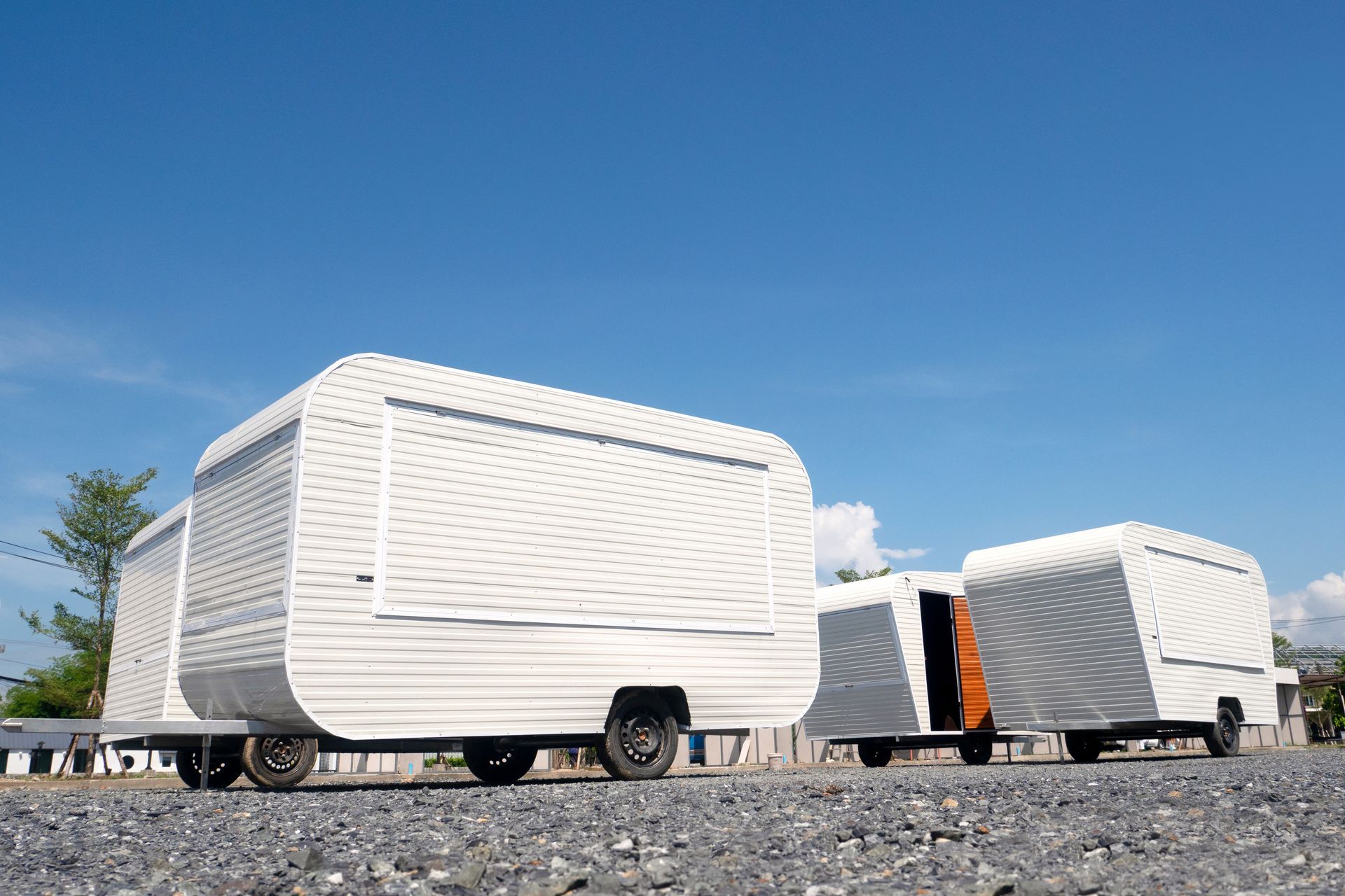 Covered trailers parked on a gravel lot under a blue sky
