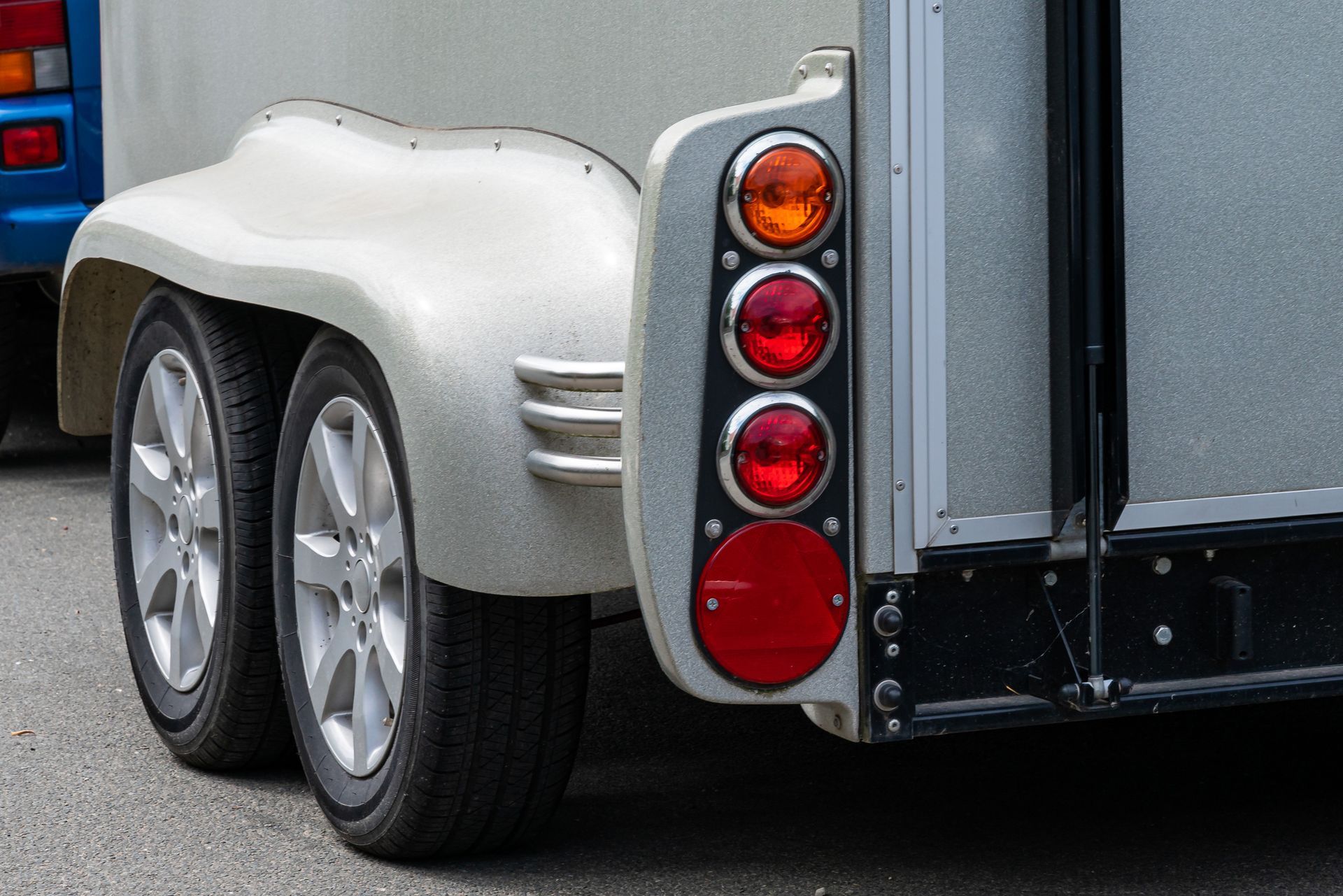 Close-up of a silver trailer with dual wheels and vertical red taillights on the rear corner