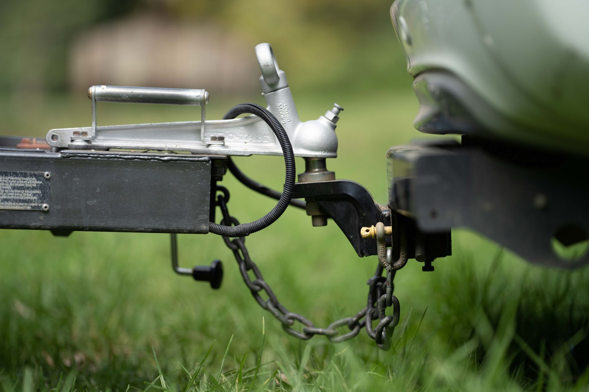 Close-up of a trailer hitch and chain attached to a green vehicle on grass