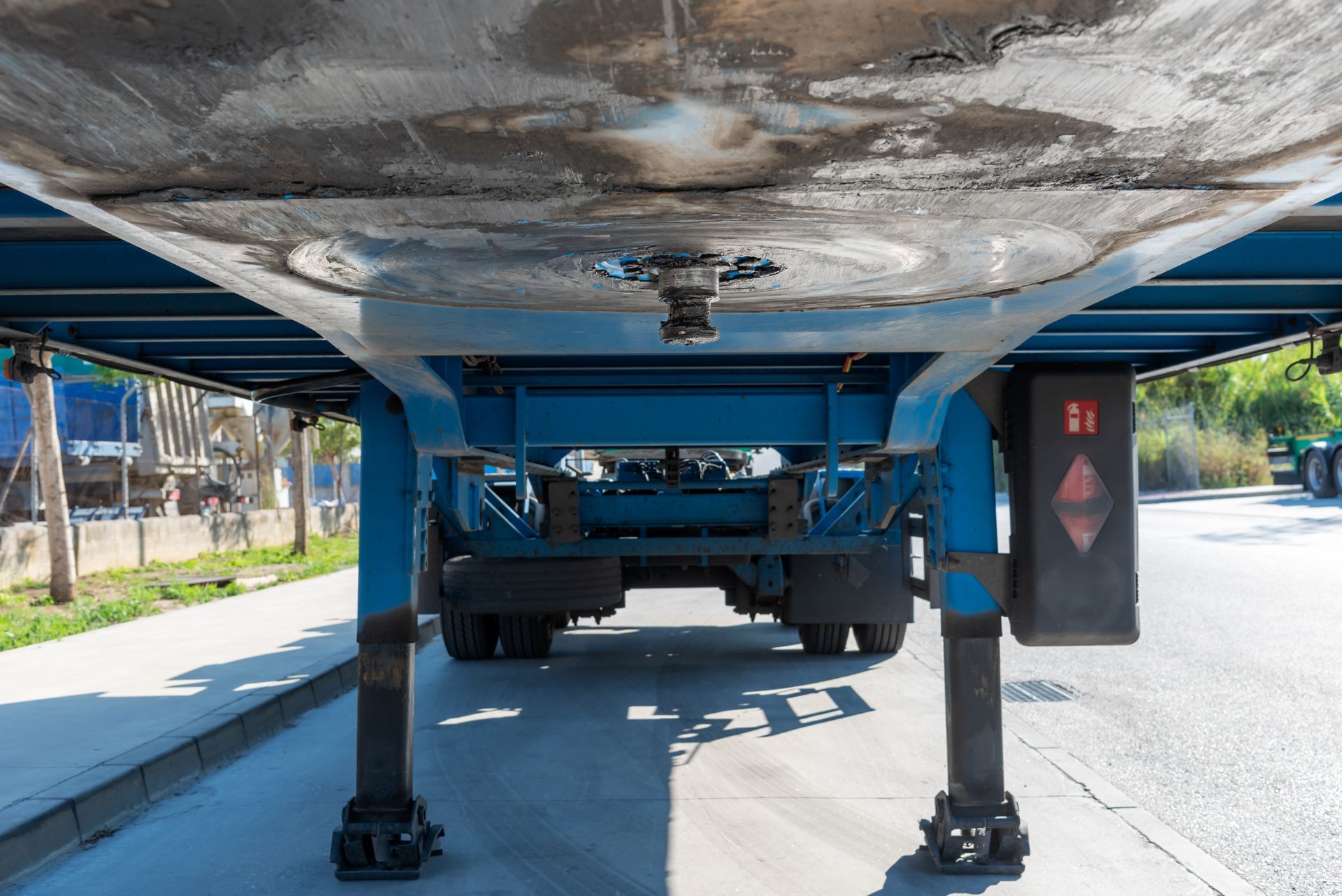 Undercarriage view of a blue trailer, showing its wheels and support legs on a paved road.