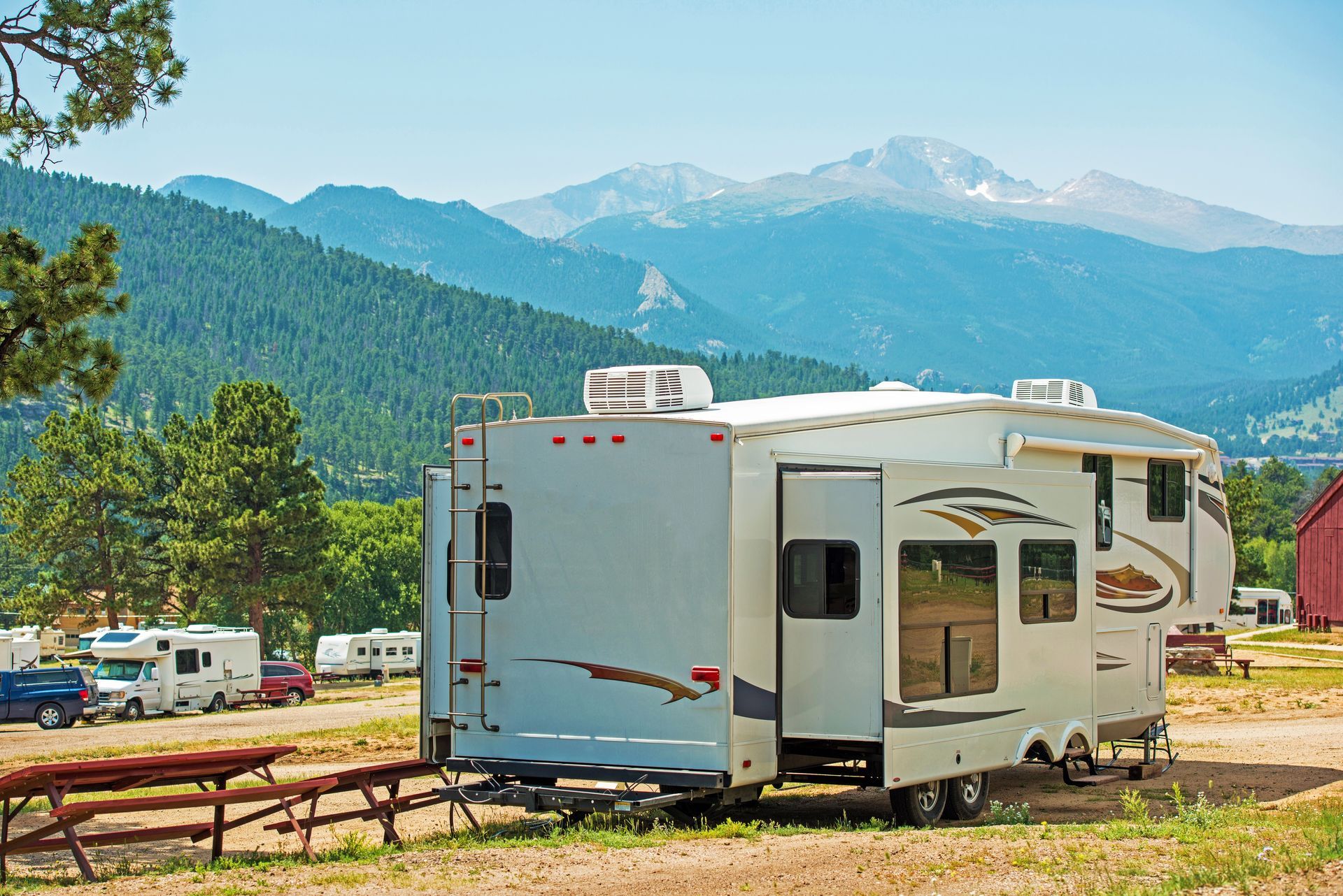 RV trailer parked in a campground with mountains and trees in the background